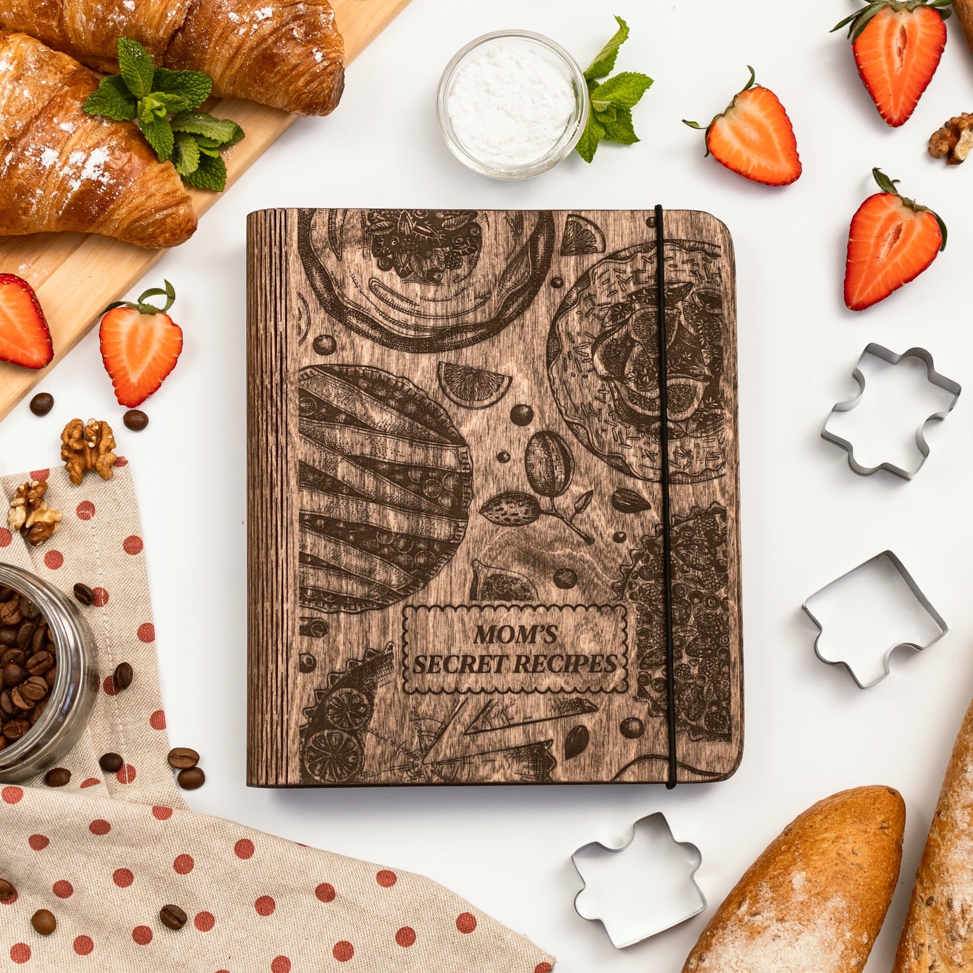 Wooden recipe book titled 'Mom's Secret Recipes' surrounded by baking ingredients on a white surface.