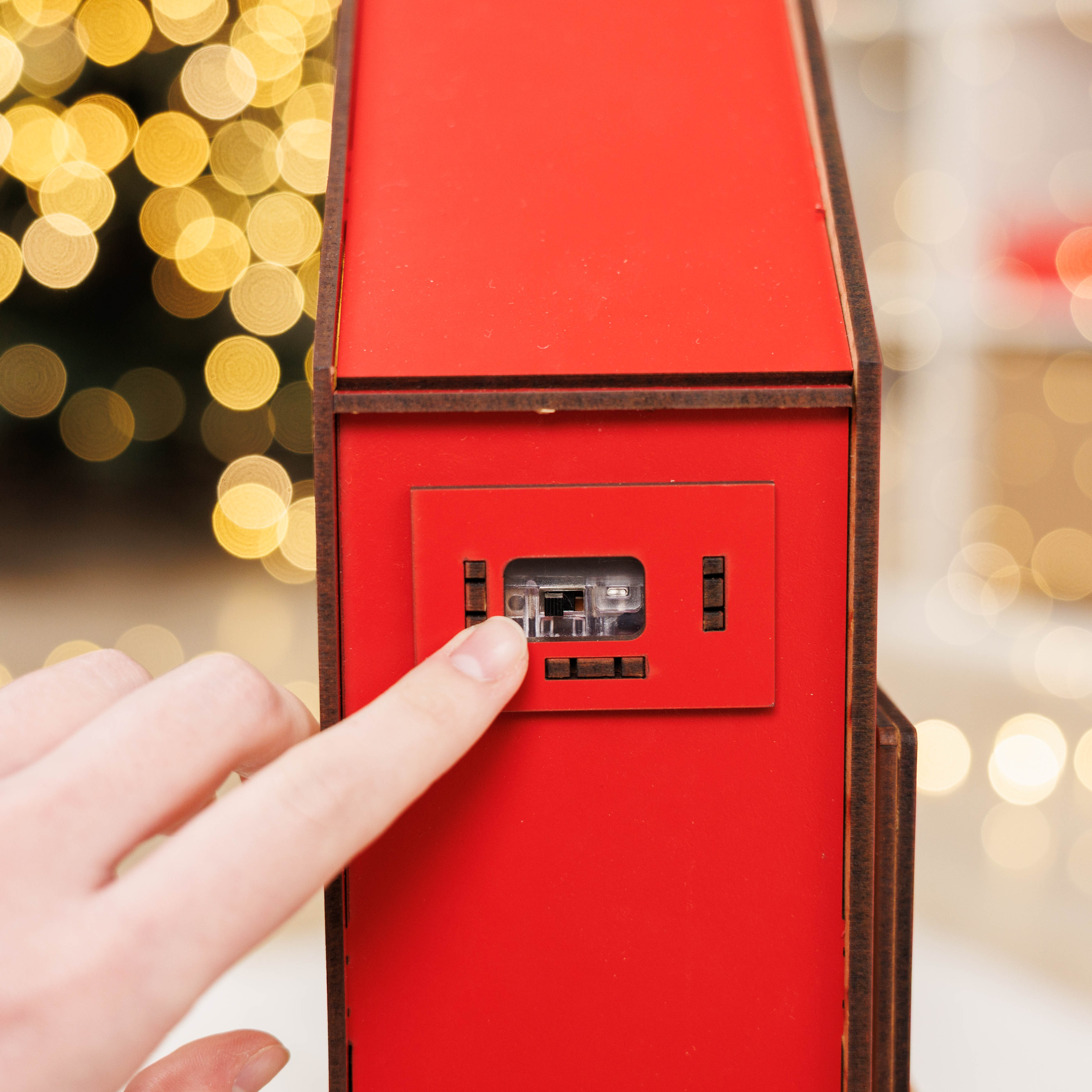 Red electronic device with a hand interacting with it against a blurred festive background