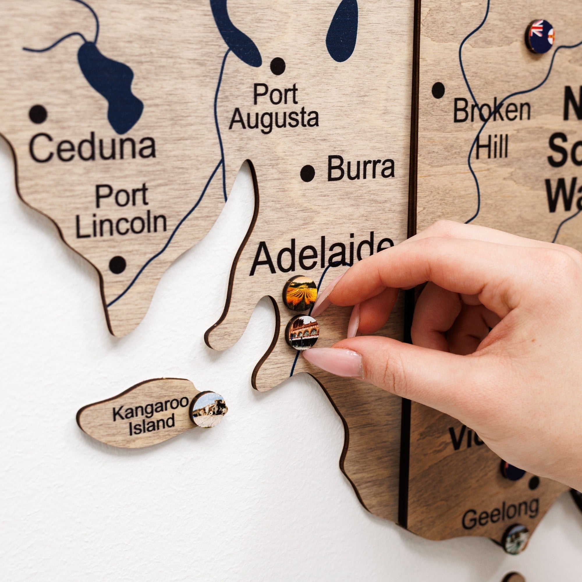 Wooden map of Australia with a hand placing a small wooden object on it.