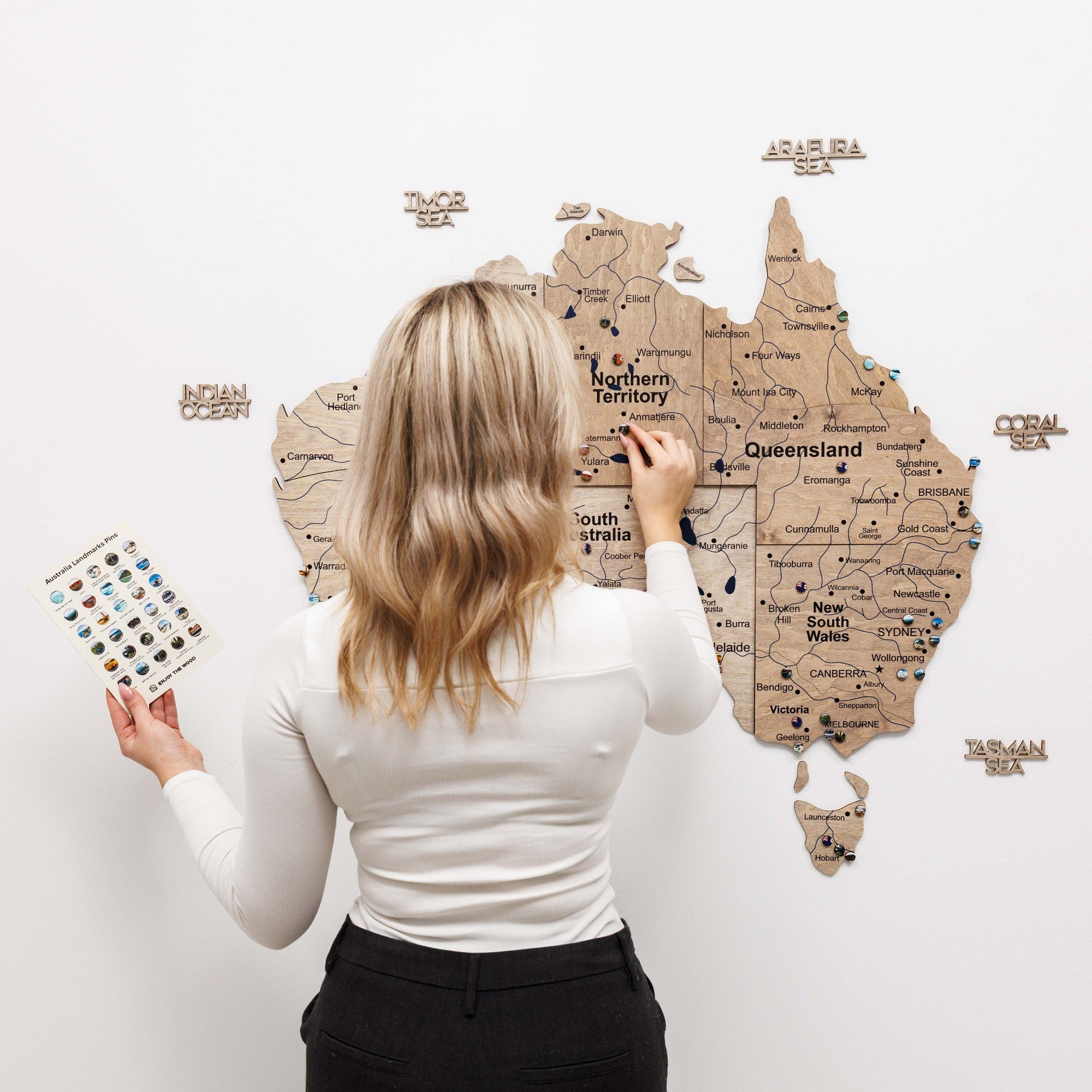 Woman interacting with a wooden map of Australia on a white wall