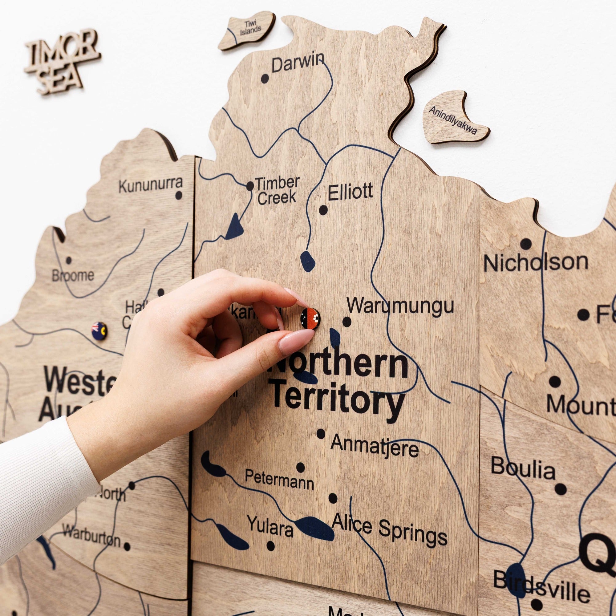 Wooden map of the Northern Territory with a hand placing a small object on it.