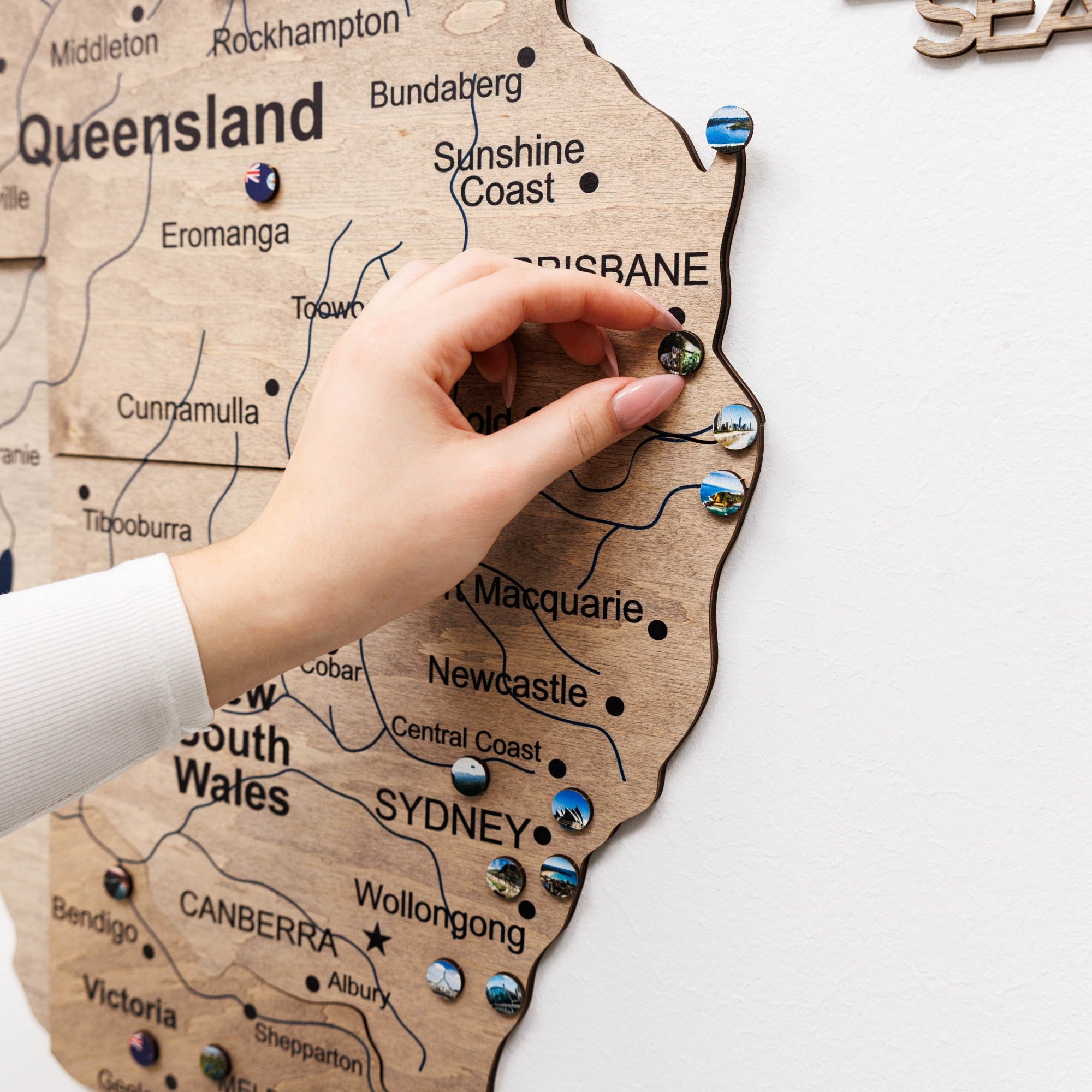 Wooden map of Australia with pins marking locations, hand placing a pin on Queensland.