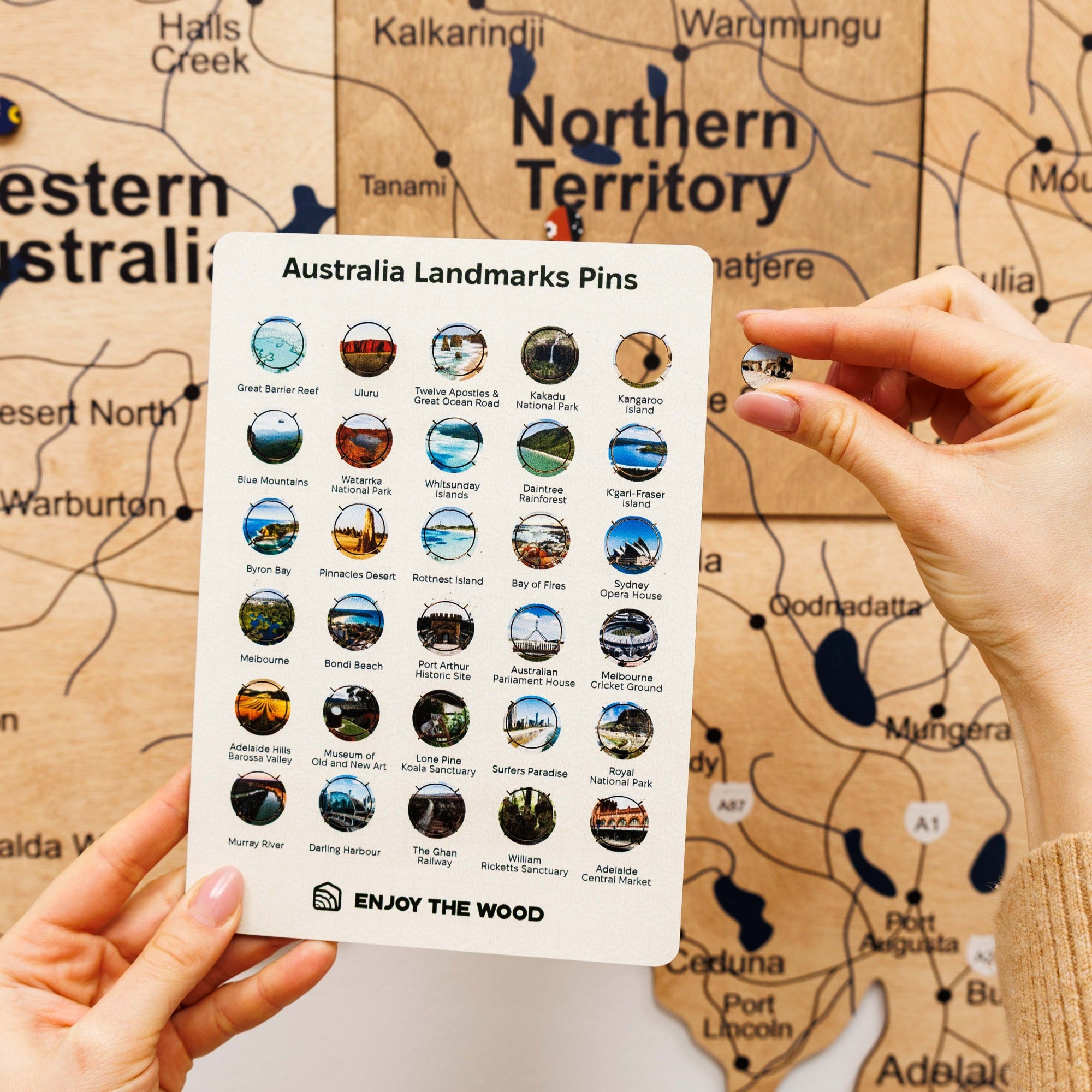 Hand holding a card with Australia landmarks pins against a map background