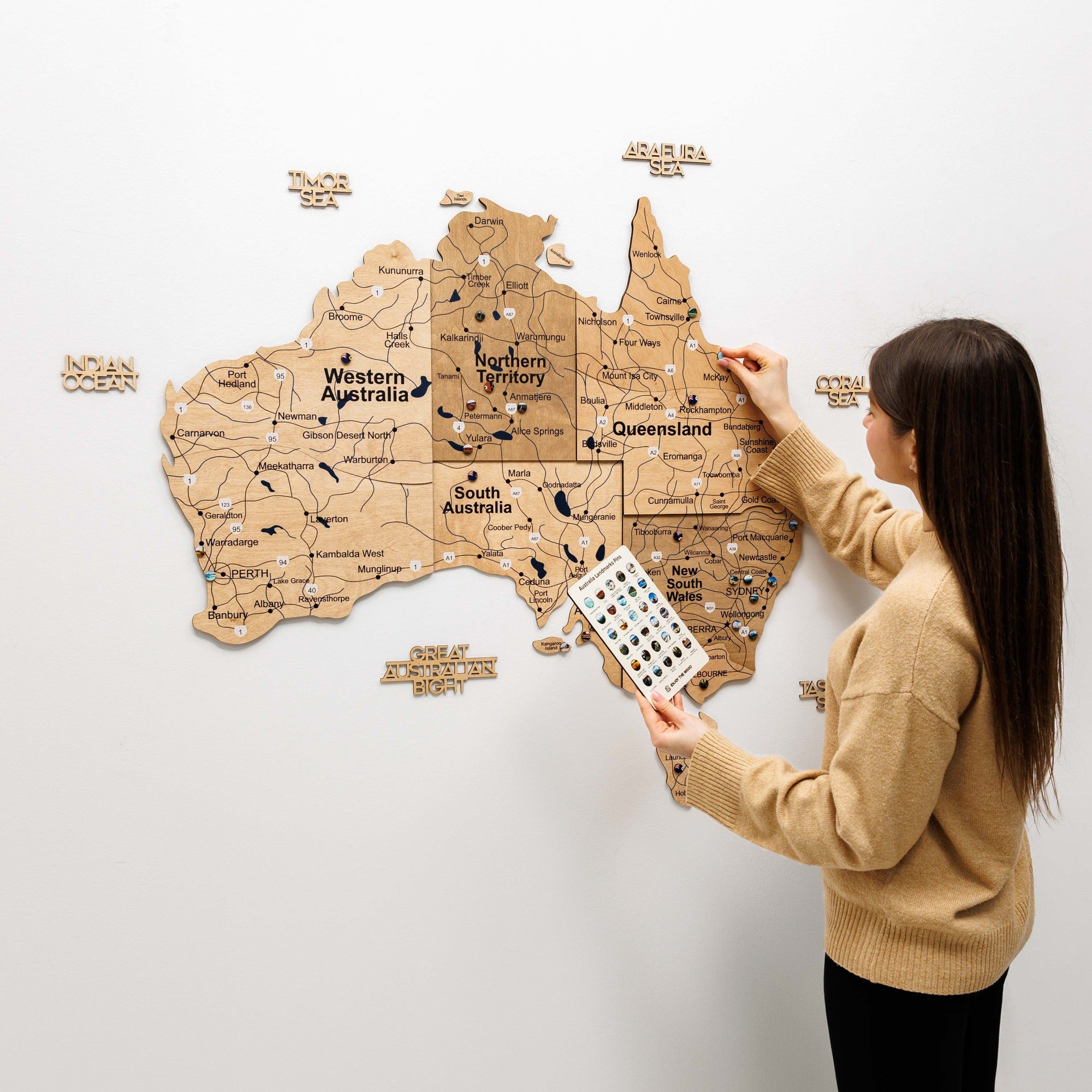Woman interacting with a wooden map of Australia on a white wall
