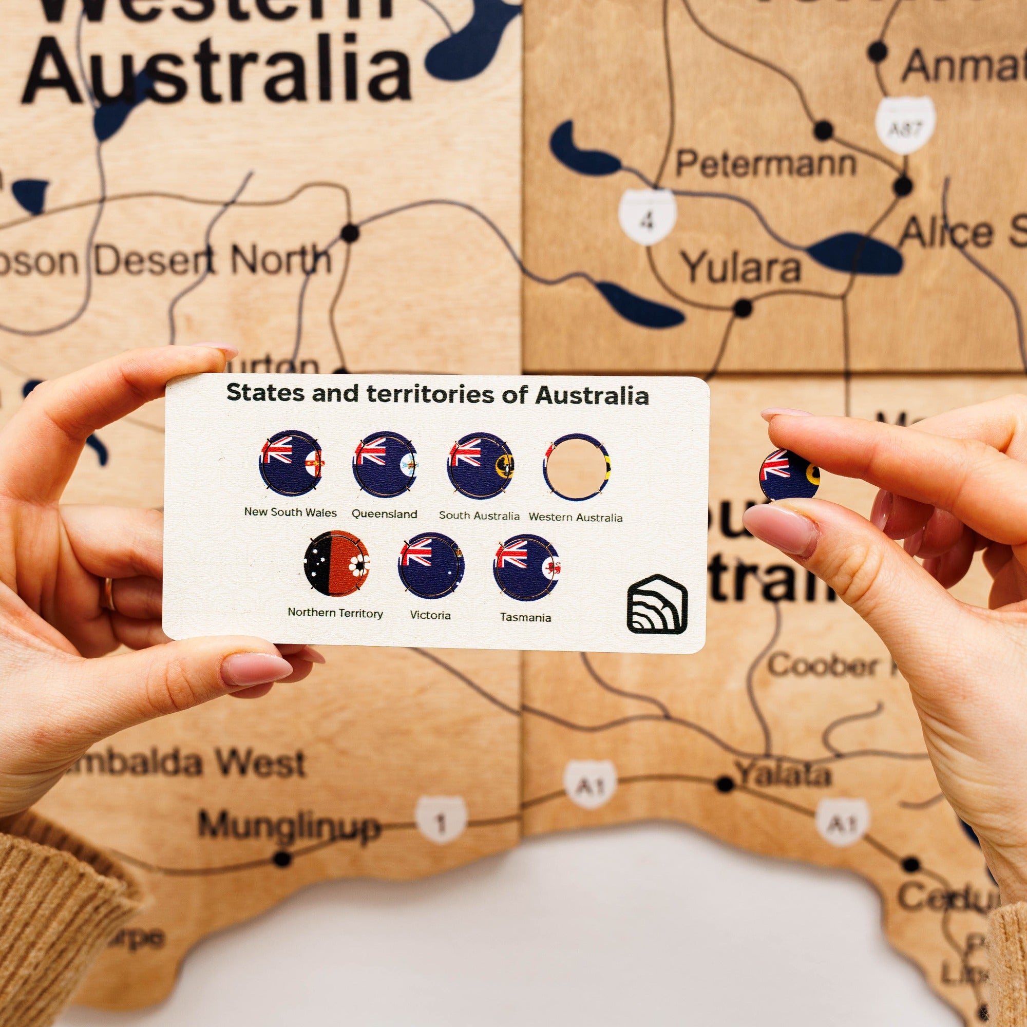 Map of Western Australia with a card displaying Australian states and territories flags held by hands.
