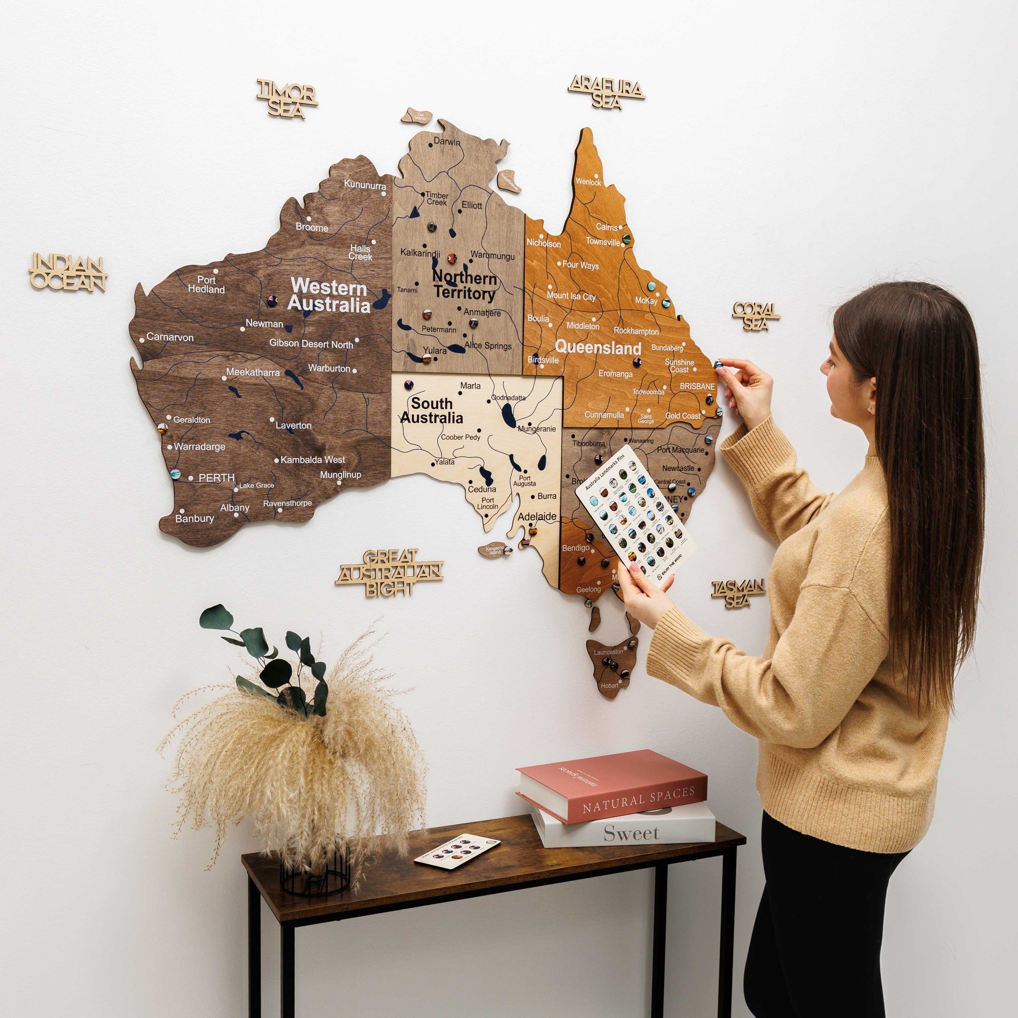 Woman interacting with a wooden map of Australia on a white wall.