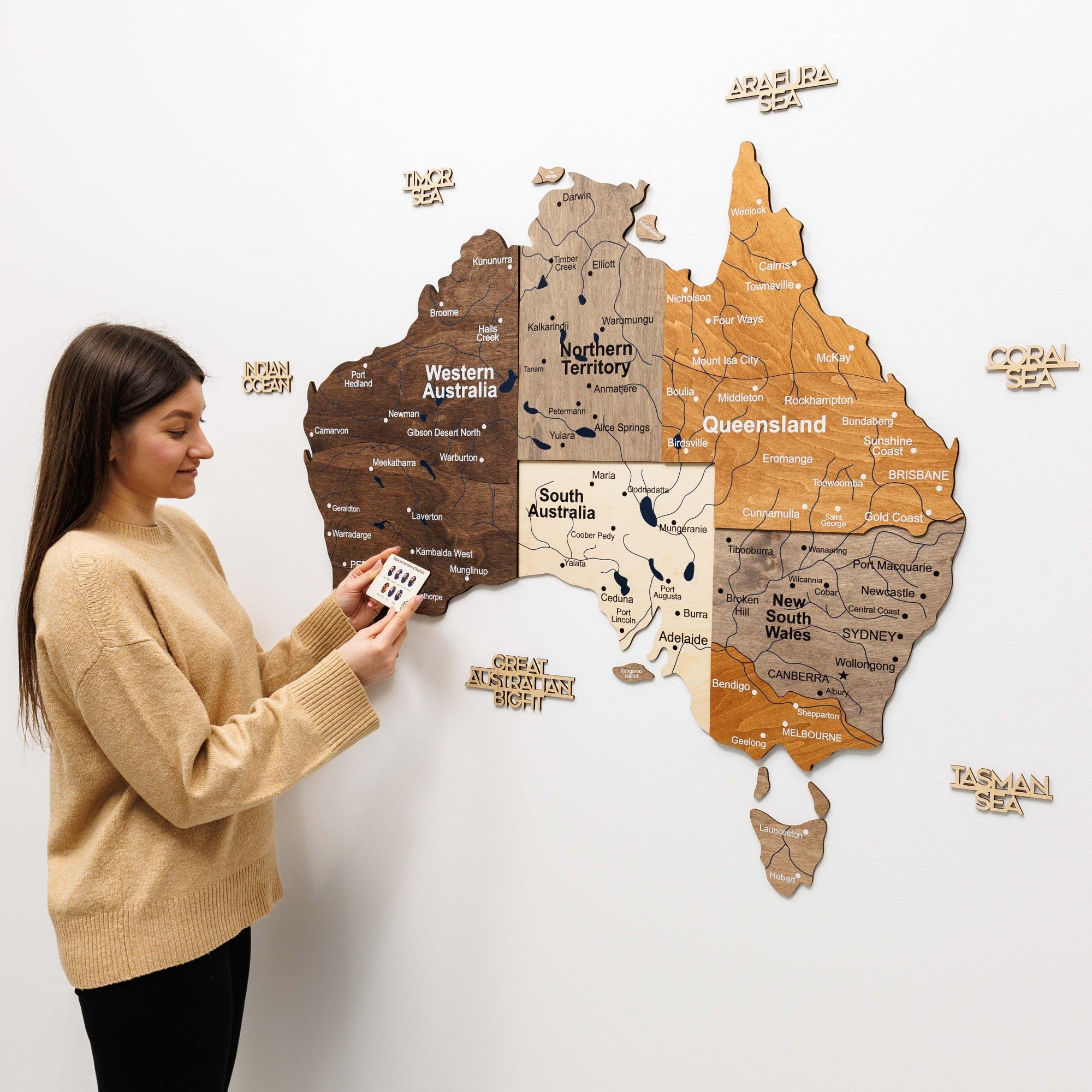 Woman interacting with a wooden map of Australia on a white wall