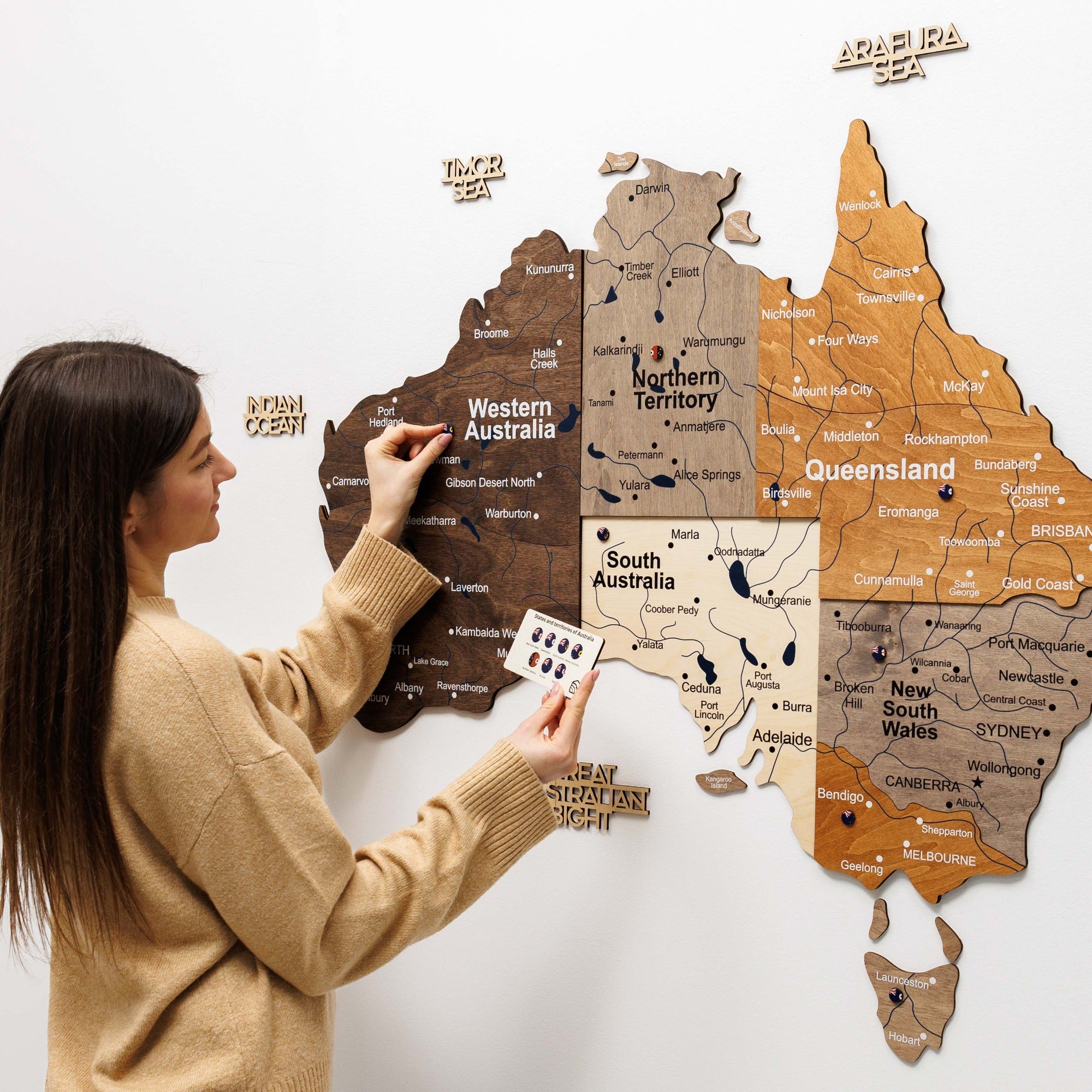 Woman interacting with a wooden map of Australia on a white wall
