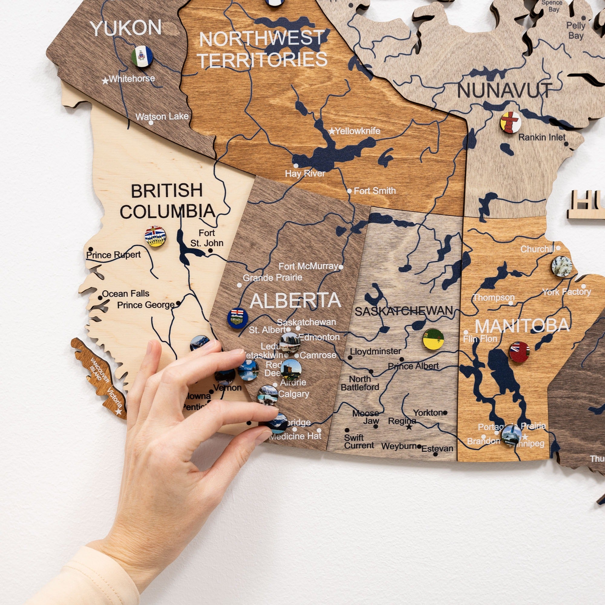 Wooden map of Canada with a hand placing a wooden piece on Alberta.