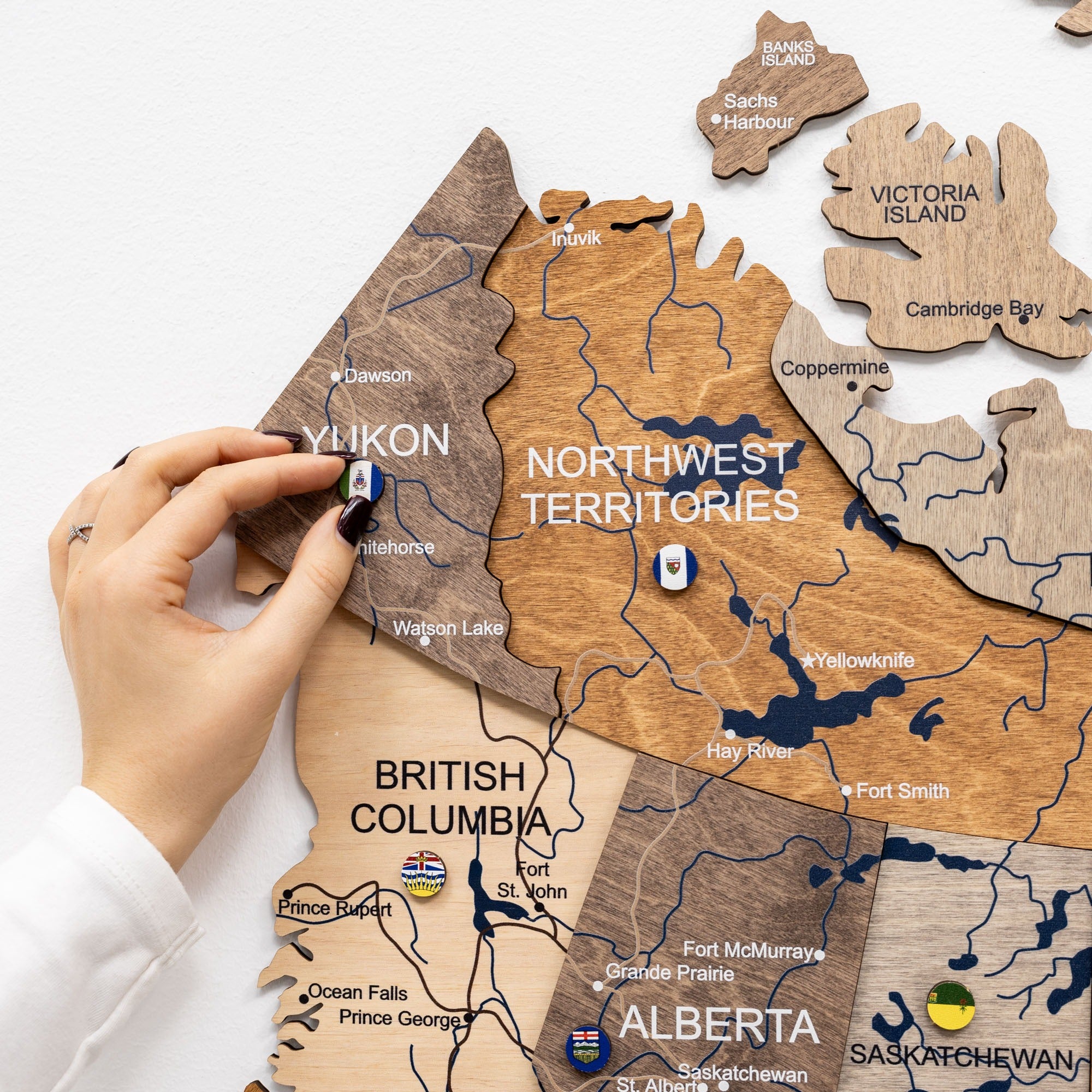 Wooden map of Canada with a hand placing a small flag on the Northwest Territories.