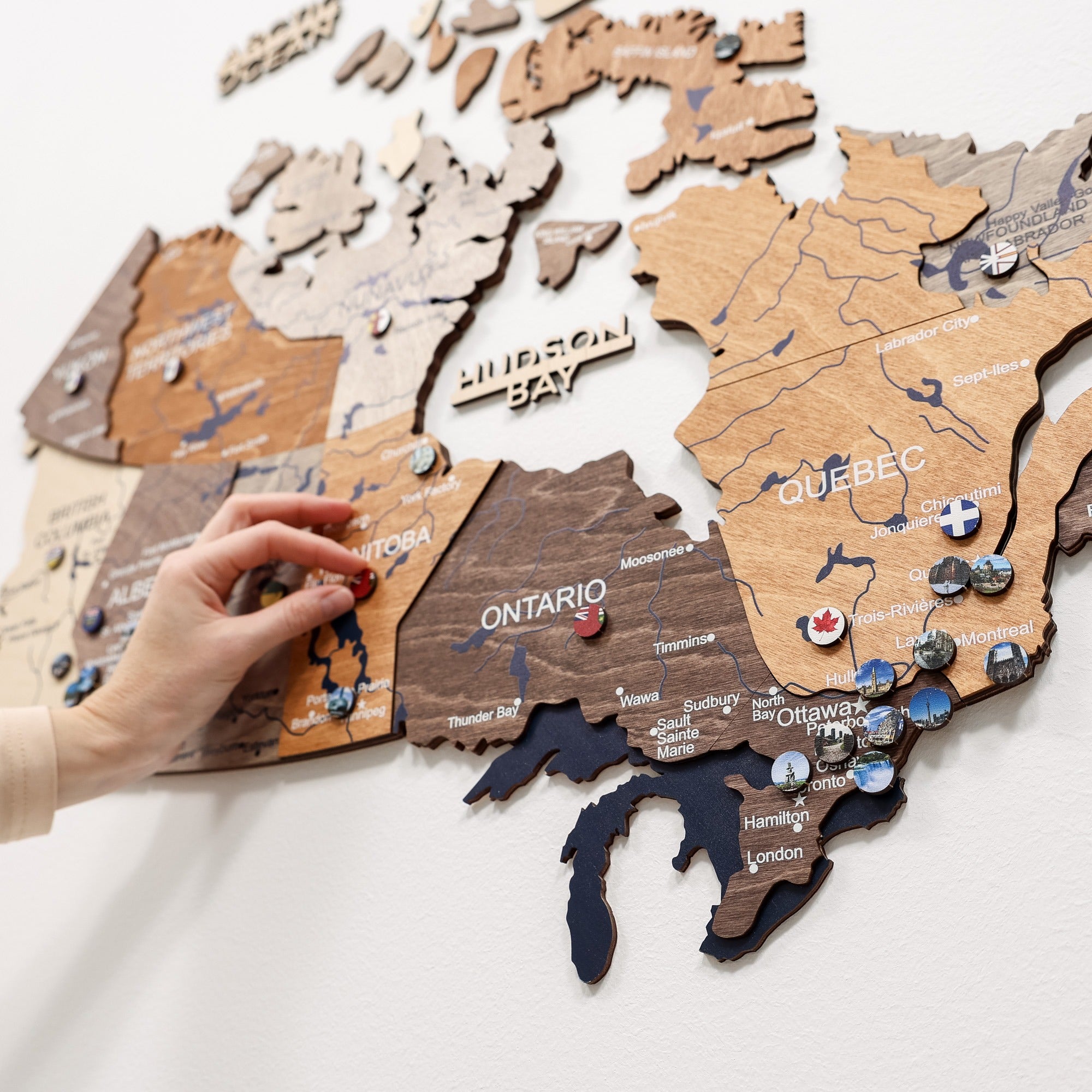 Wooden puzzle map of Canada with a hand placing a piece on a white surface.