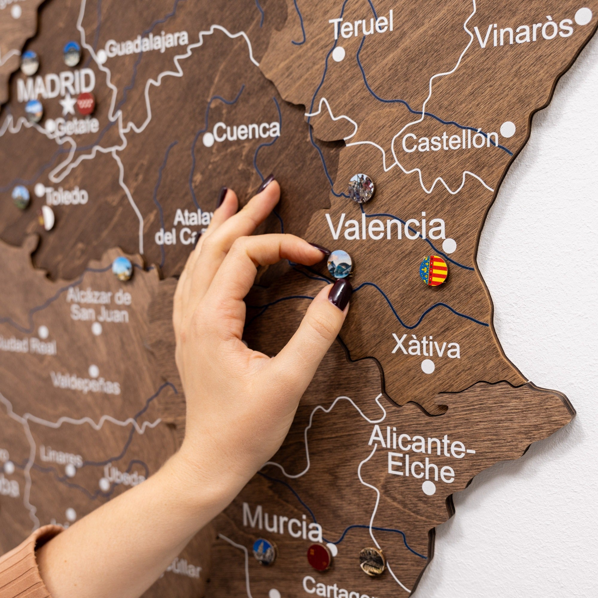 Hand placing a pin on a wooden map of Spain with Valencia highlighted.