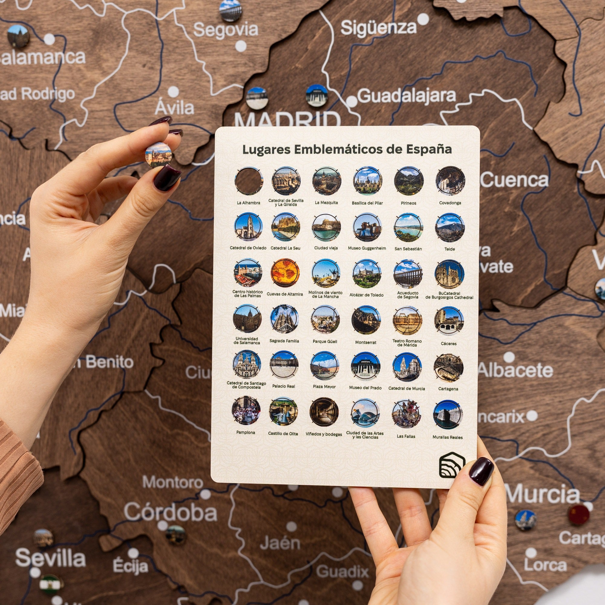 Person holding a card with icons of famous places in Spain against a wooden map of Spain.