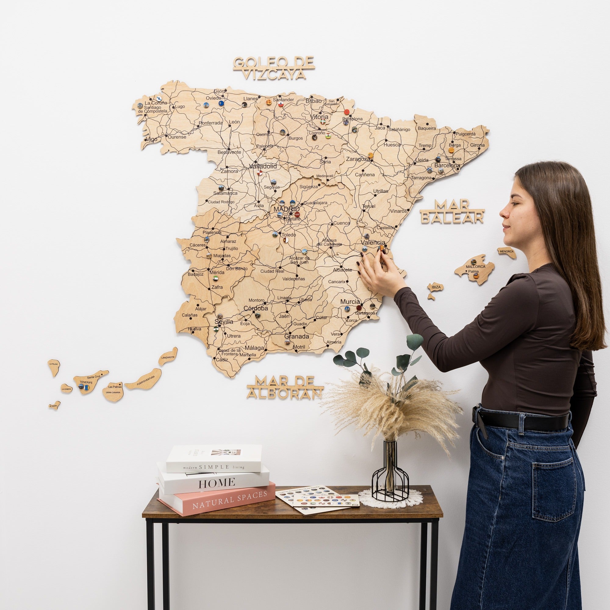 Woman interacting with a wooden map of Spain on a white wall.