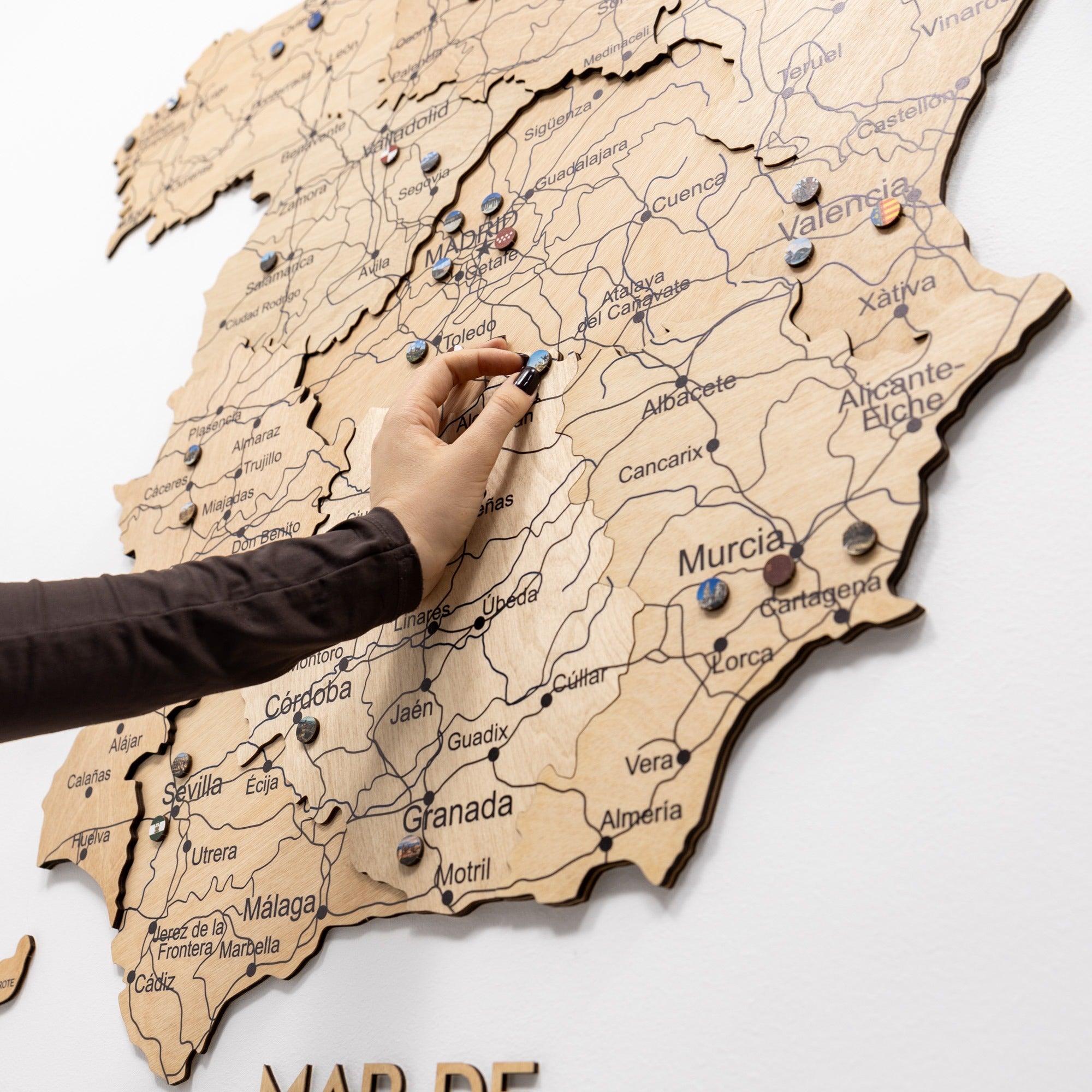 Hand placing a pin on a wooden map of Spain