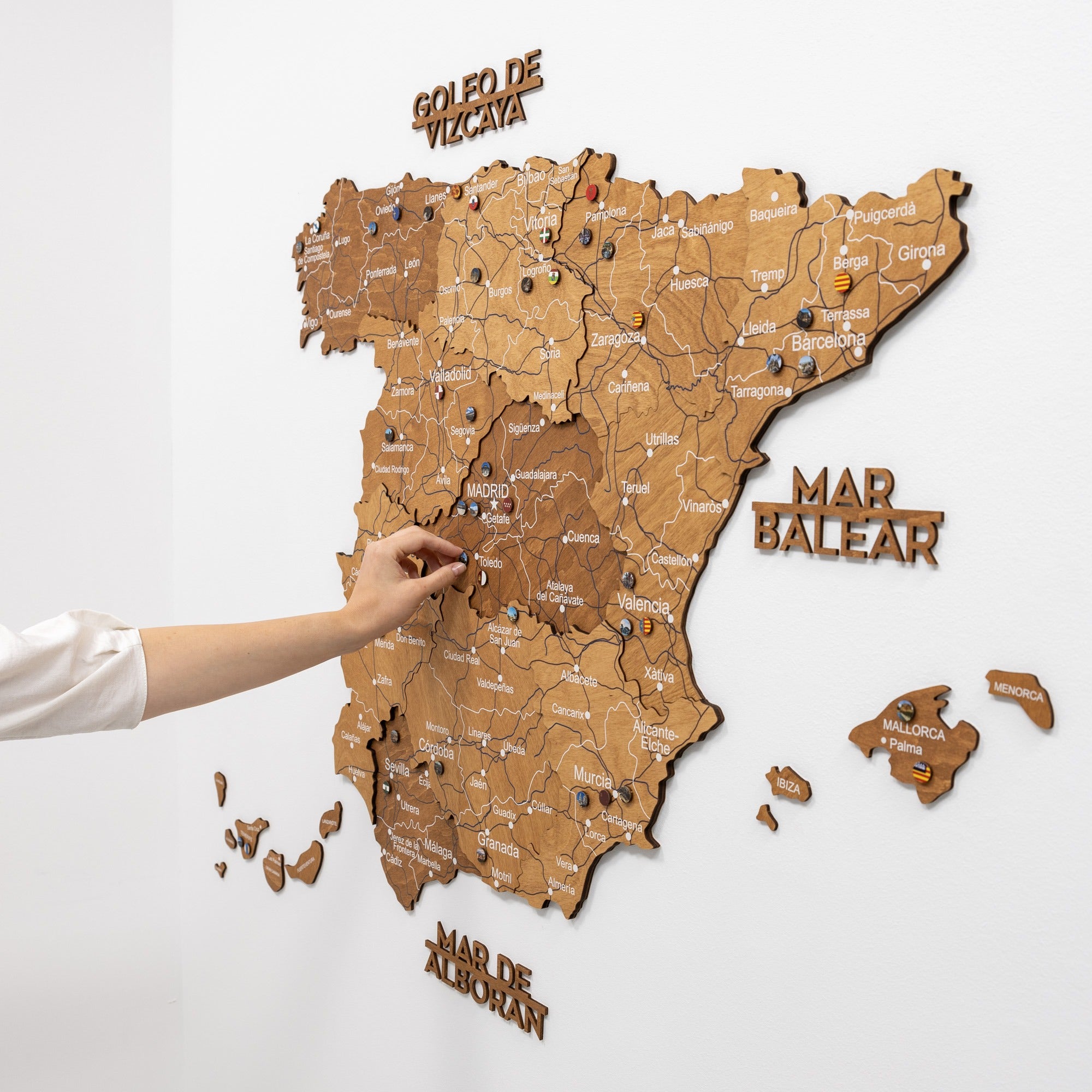 Wooden map of Spain with a hand pointing to a location on the map.