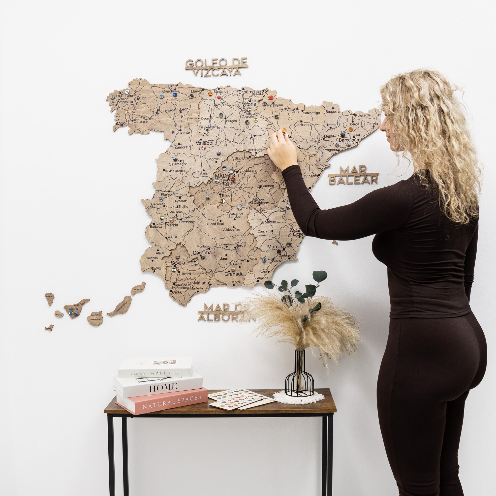 Woman interacting with a wooden map of Spain on a white wall.