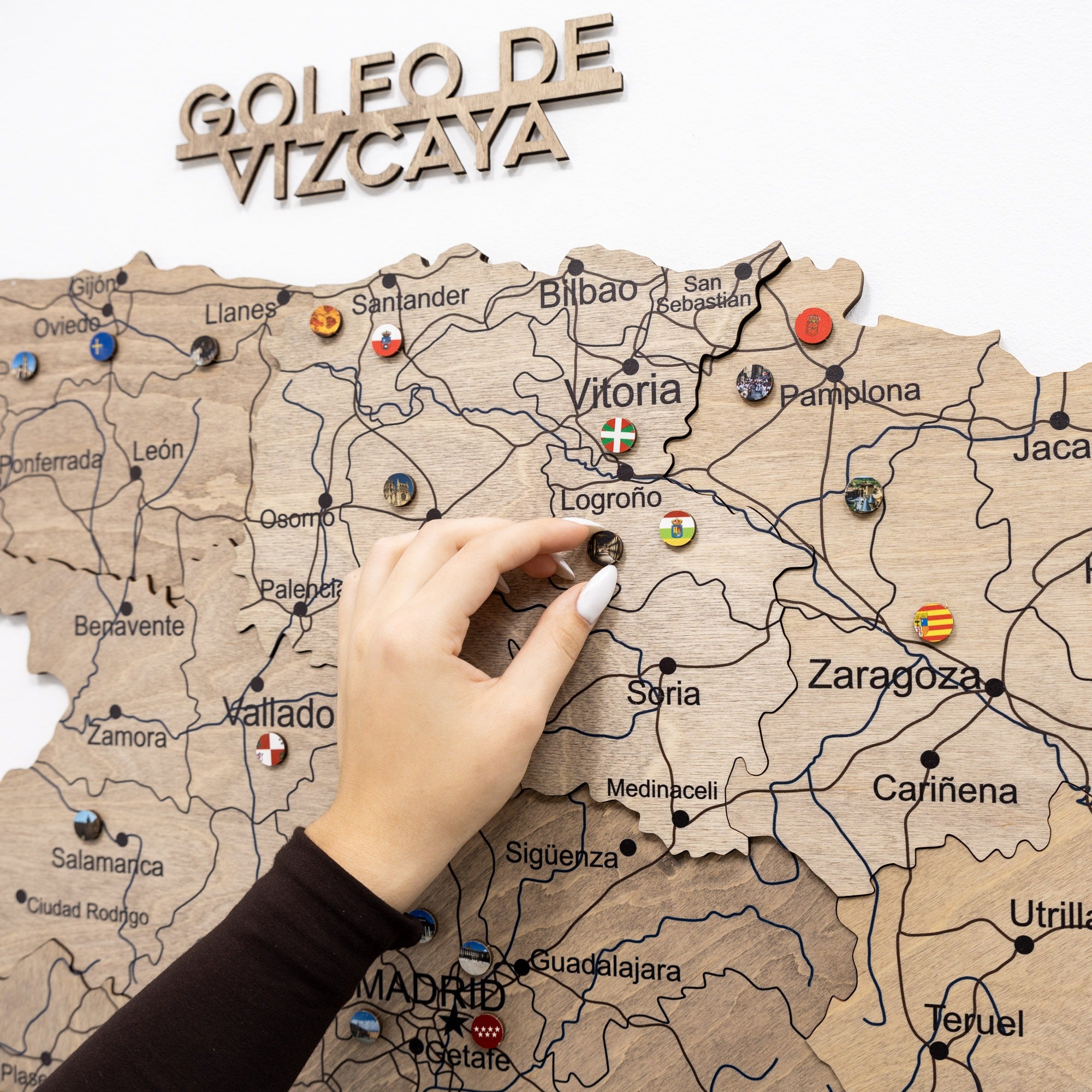 Wooden map of Spain with pins marking locations, hand pointing to Vitoria.