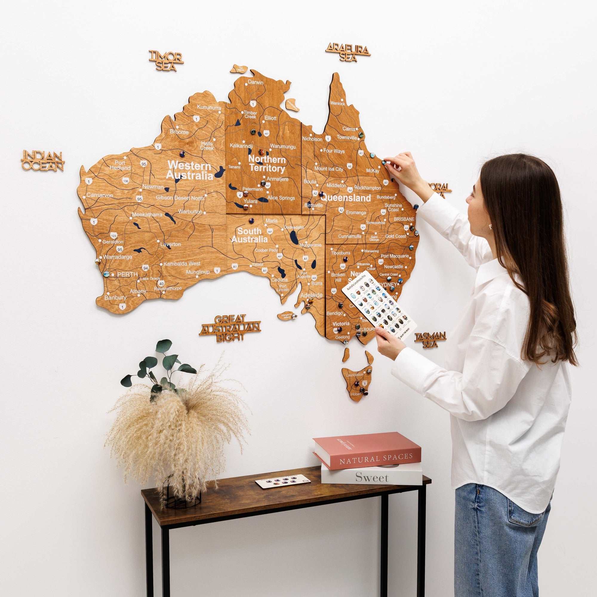 Woman interacting with a wooden map of Australia on a white wall.