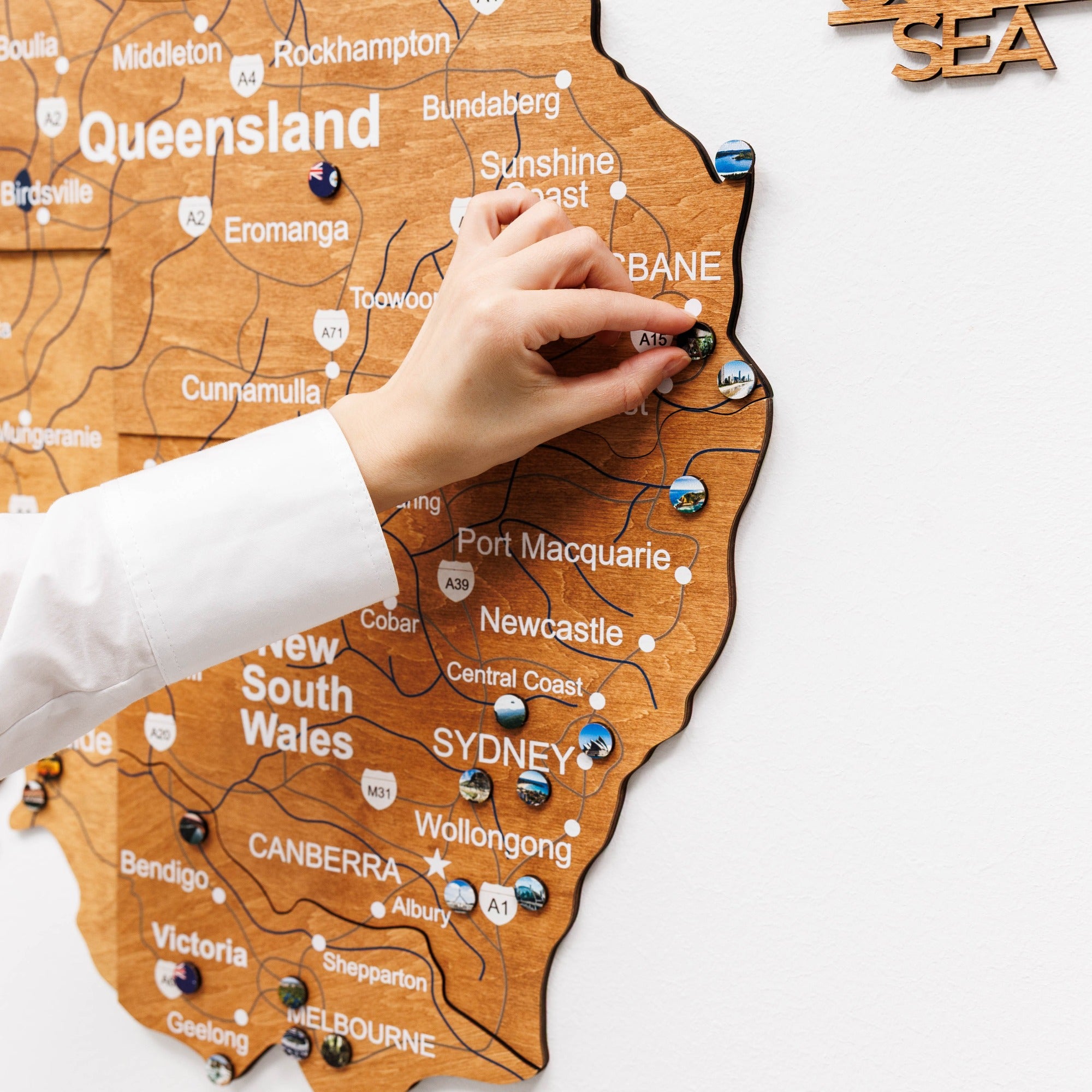 Wooden map of Australia with a hand placing a pin on Queensland