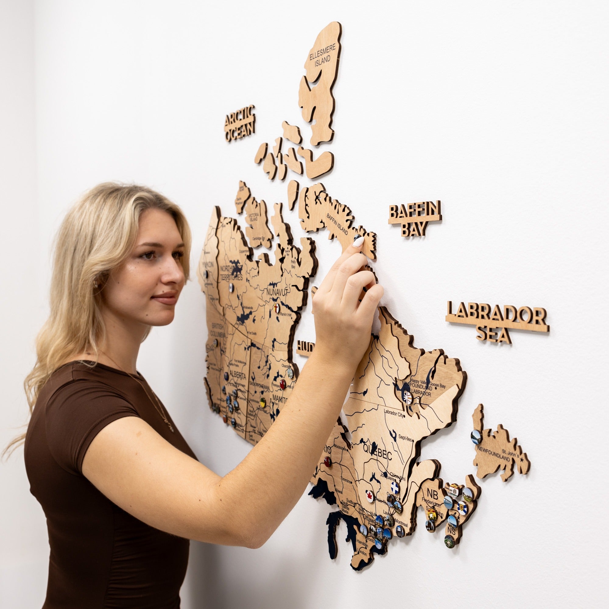 Woman interacting with a wooden map of Canada on a white wall