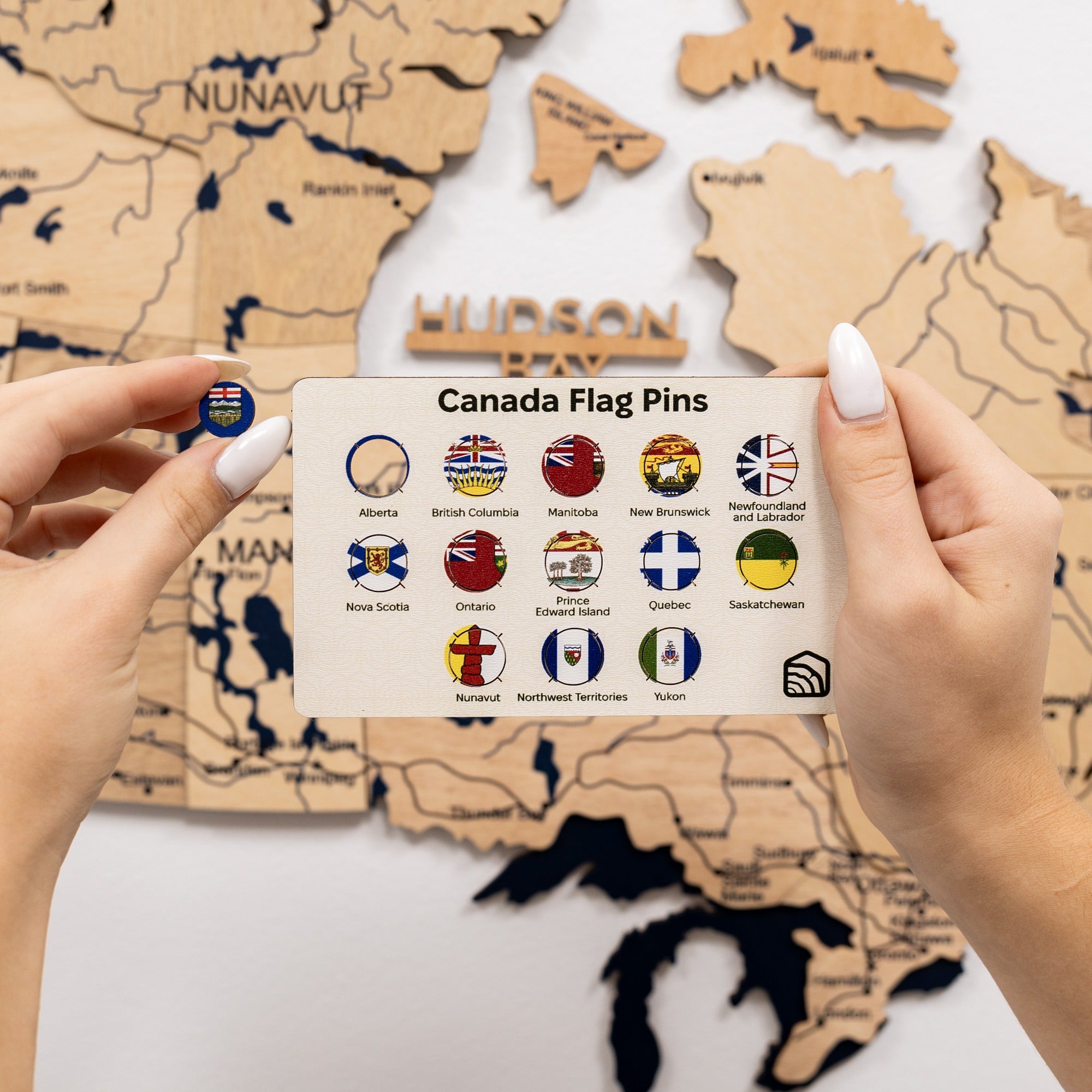 Card with Canadian flag pins held in front of a wooden map of Canada