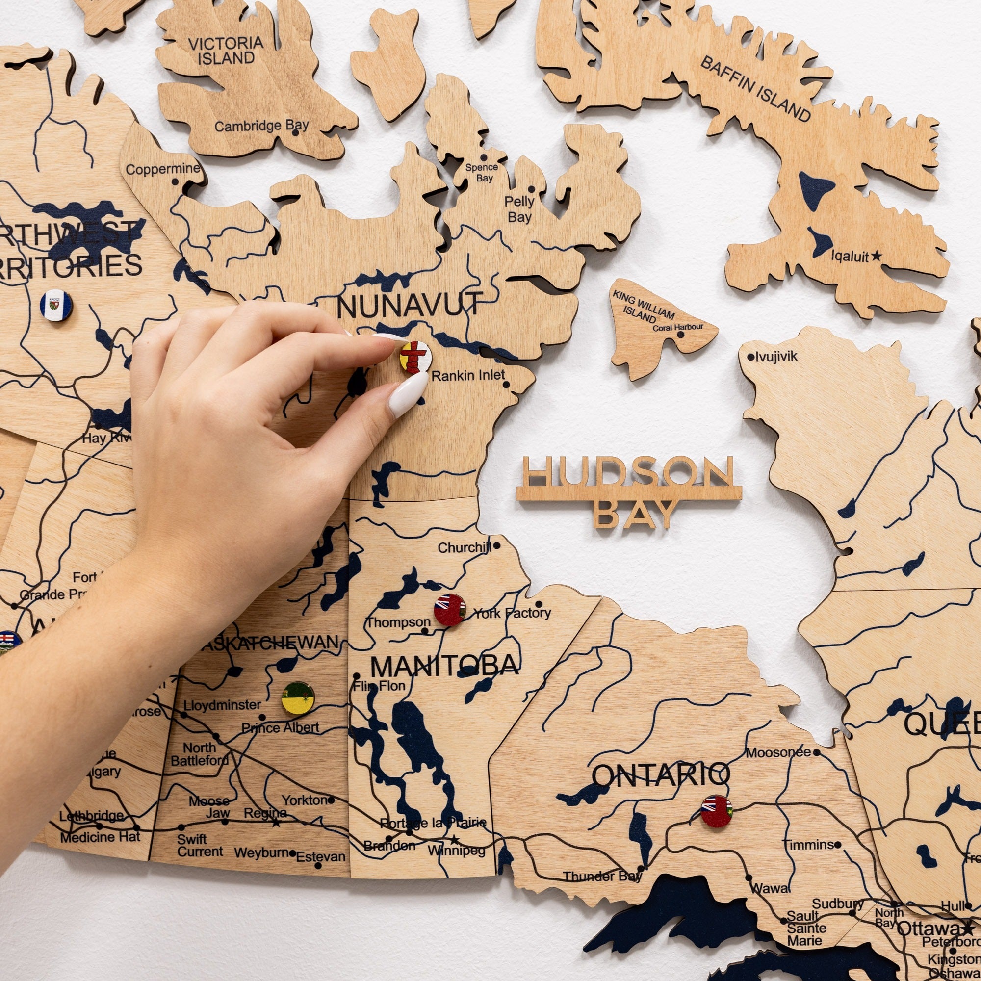 Wooden map of Canada with a hand placing a gold pin on Hudson Bay.