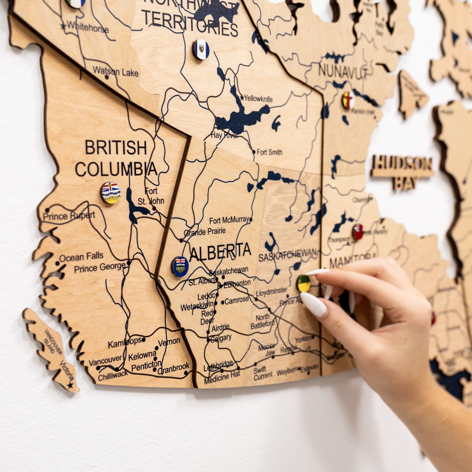Wooden map of Canada with a hand pointing to a location.