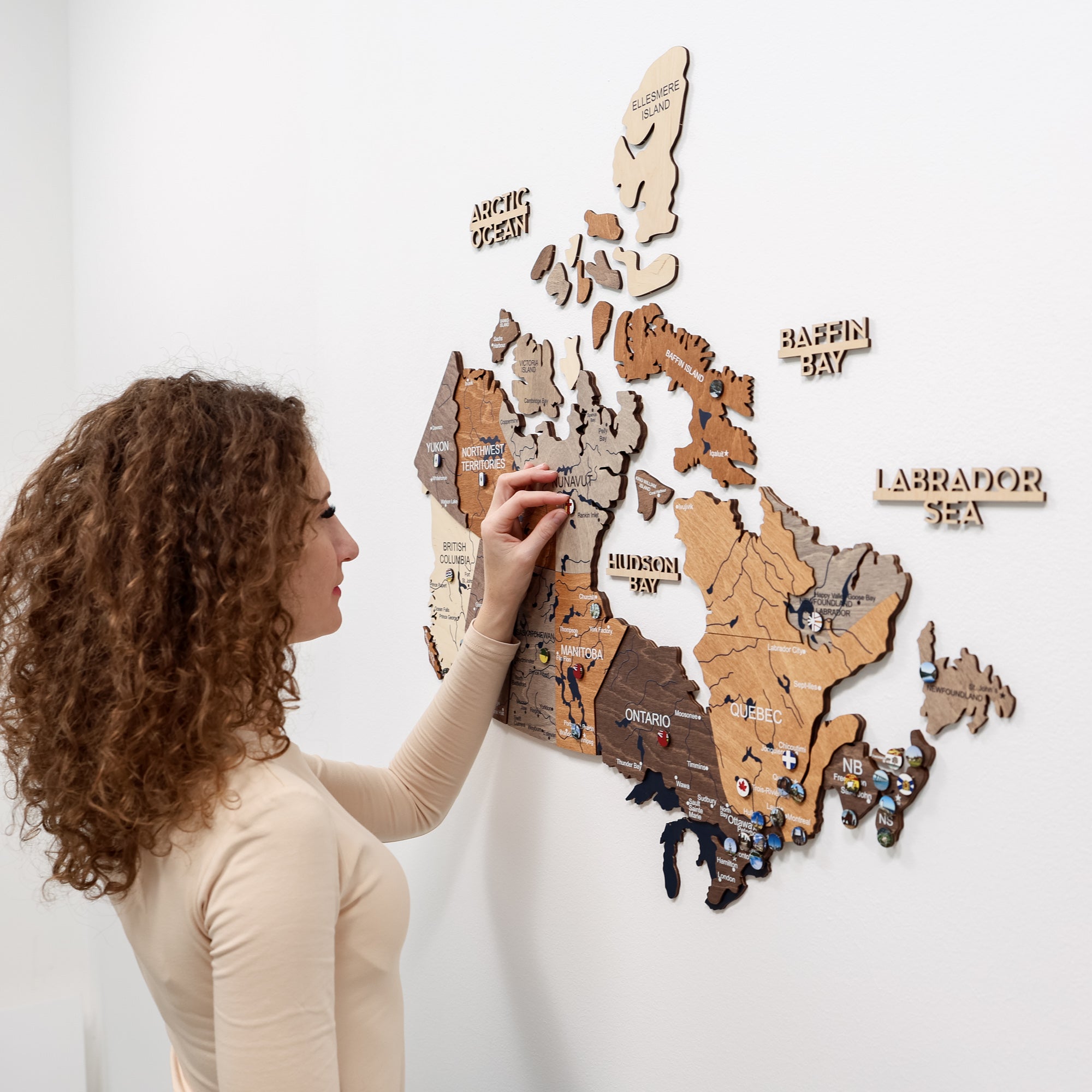 Woman interacting with a wooden map of Canada on a white wall
