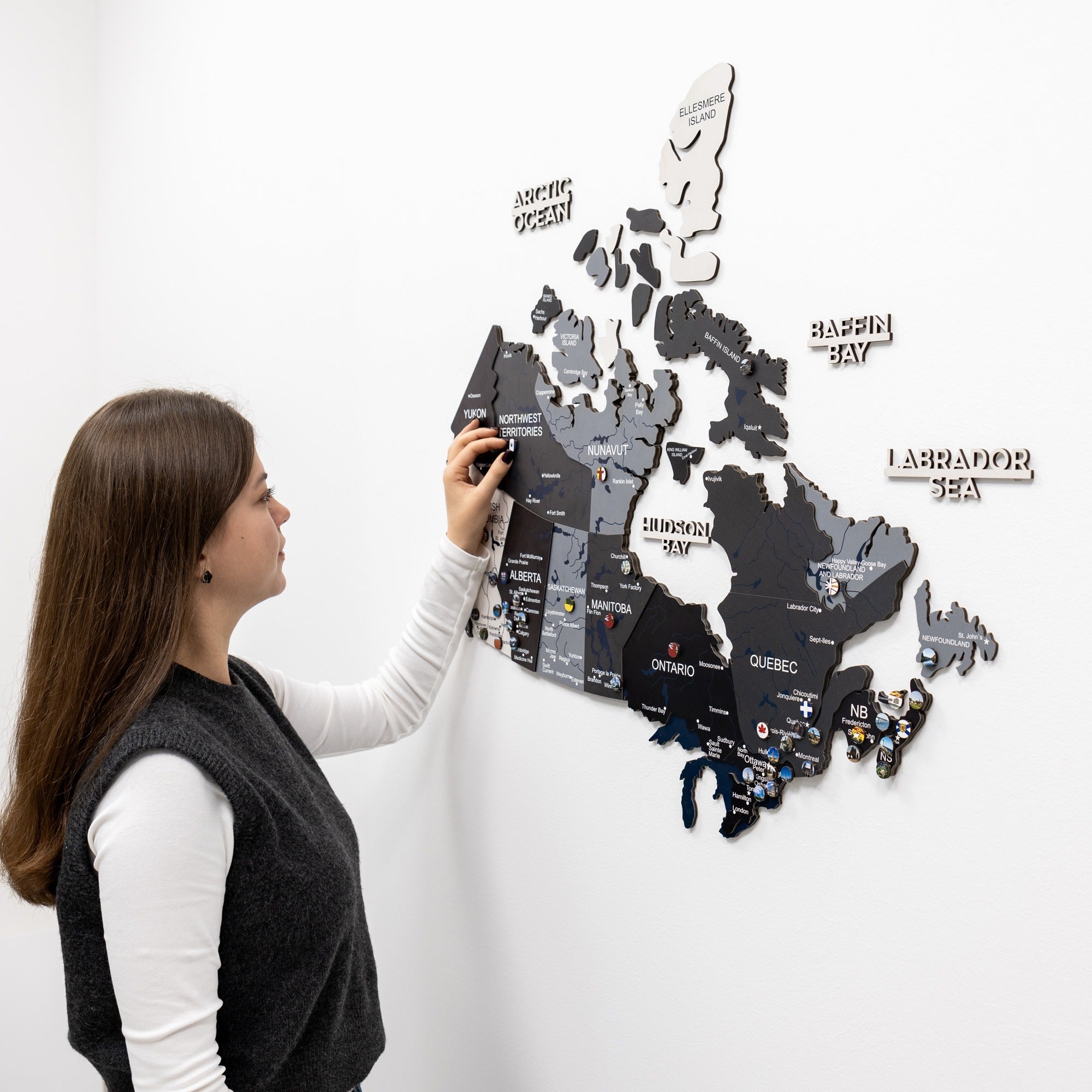 Woman interacting with a magnetic Canada map on a white wall
