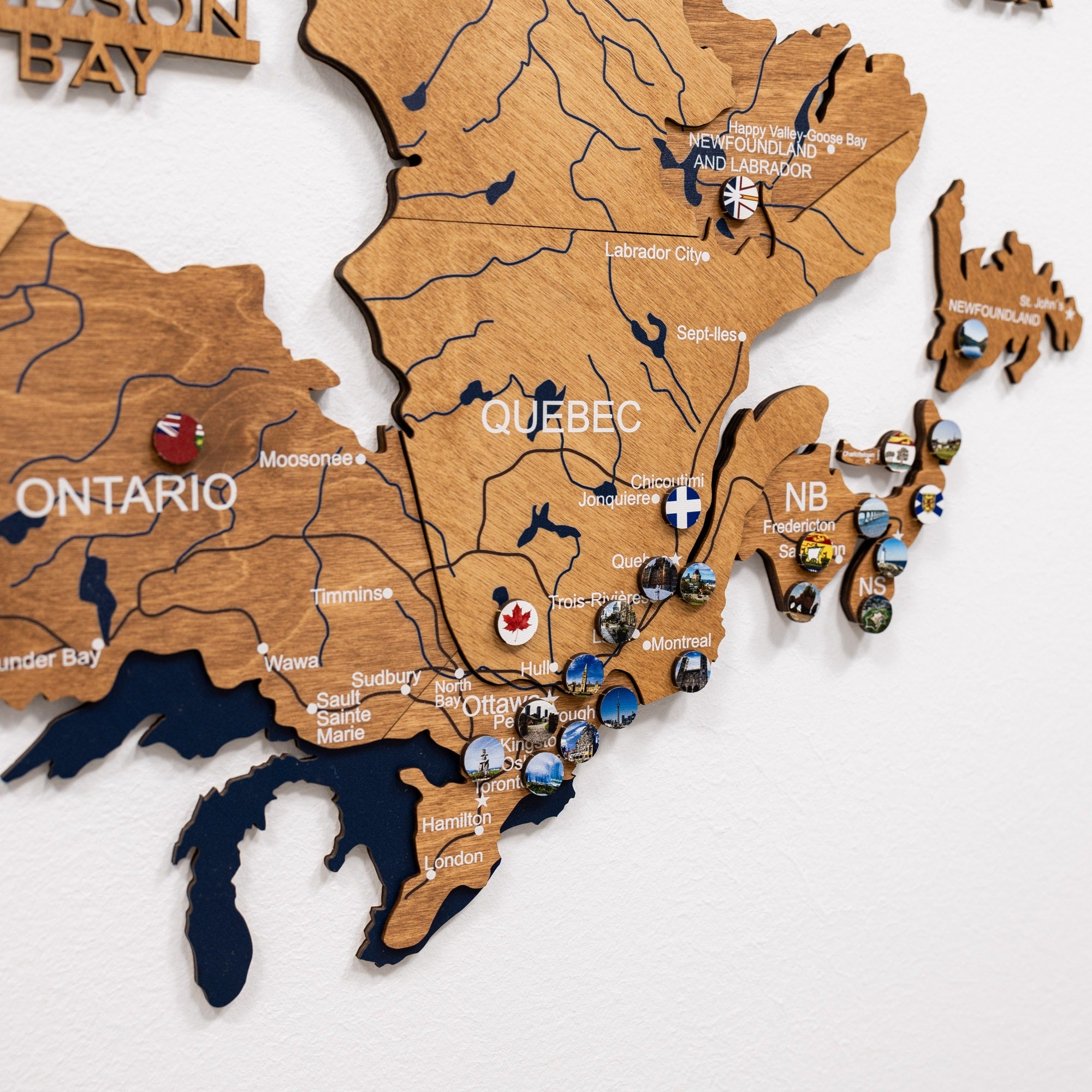 Wooden map of Canada with various pins and markers on a white background