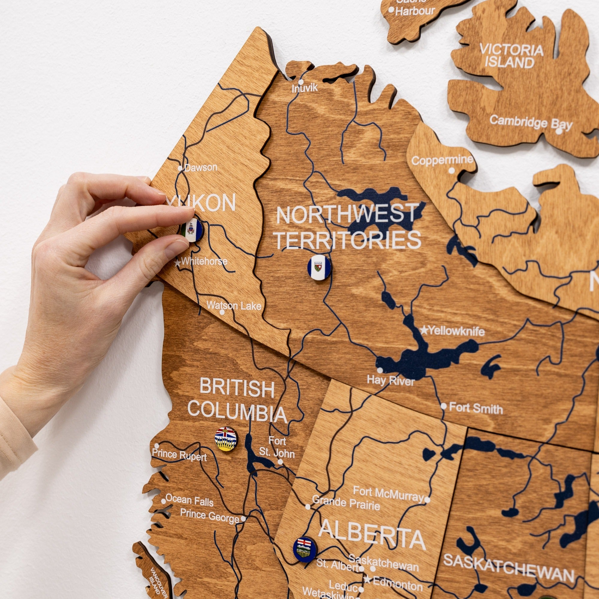 Wooden map of Canada with a hand placing a small flag on the Northwest Territories.