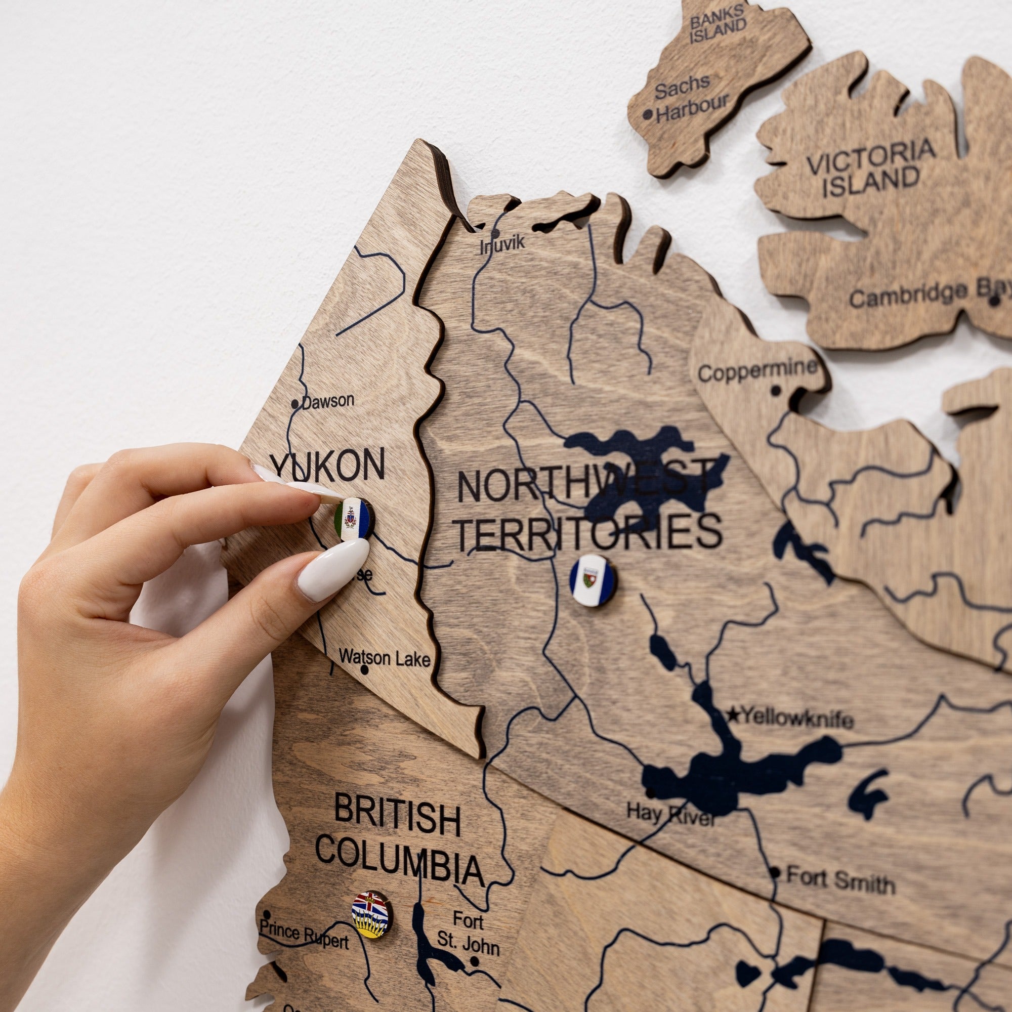Wooden map of Canada with a hand placing a small flag on British Columbia.