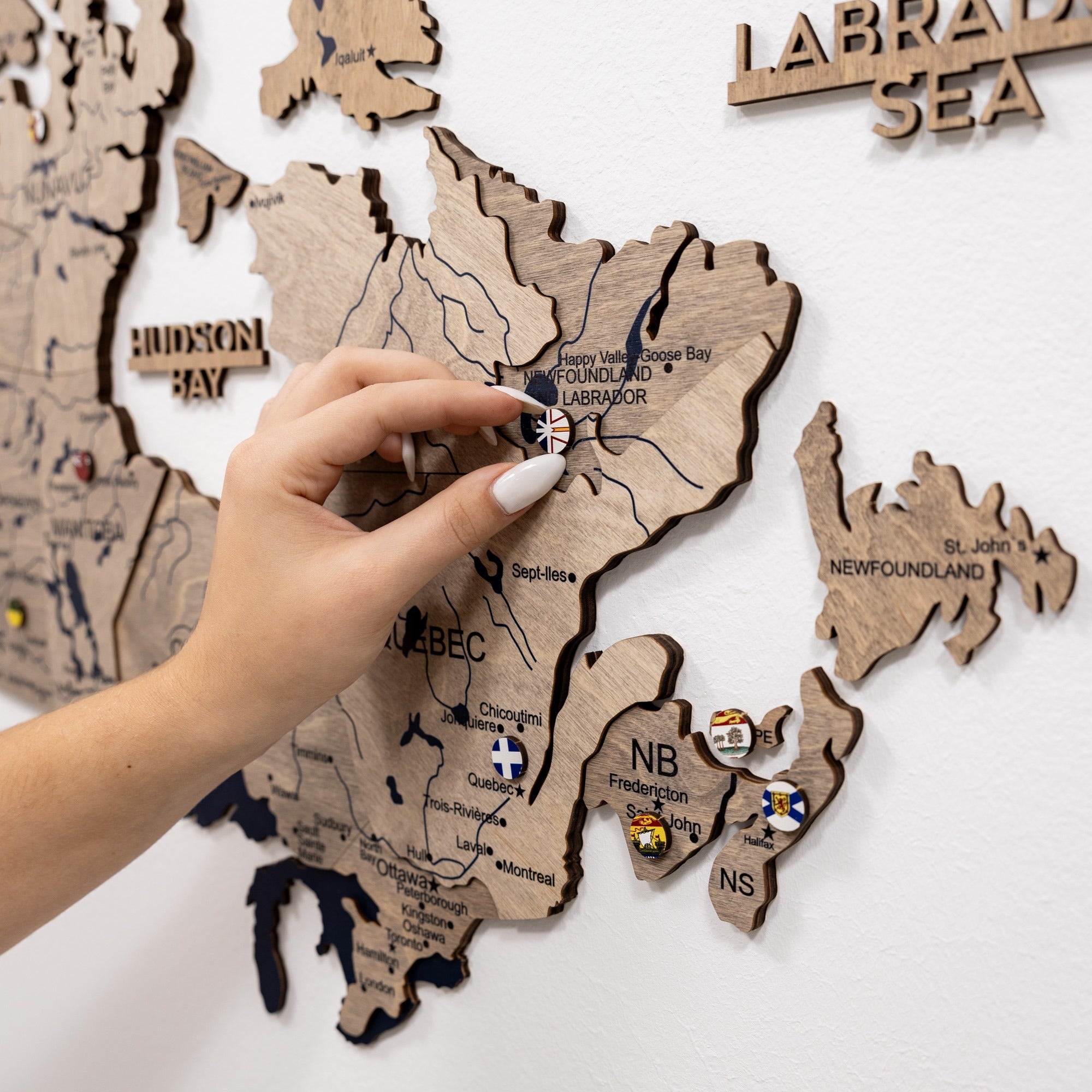 Wooden map of Canada with a hand pointing to Labrador, on a white background.