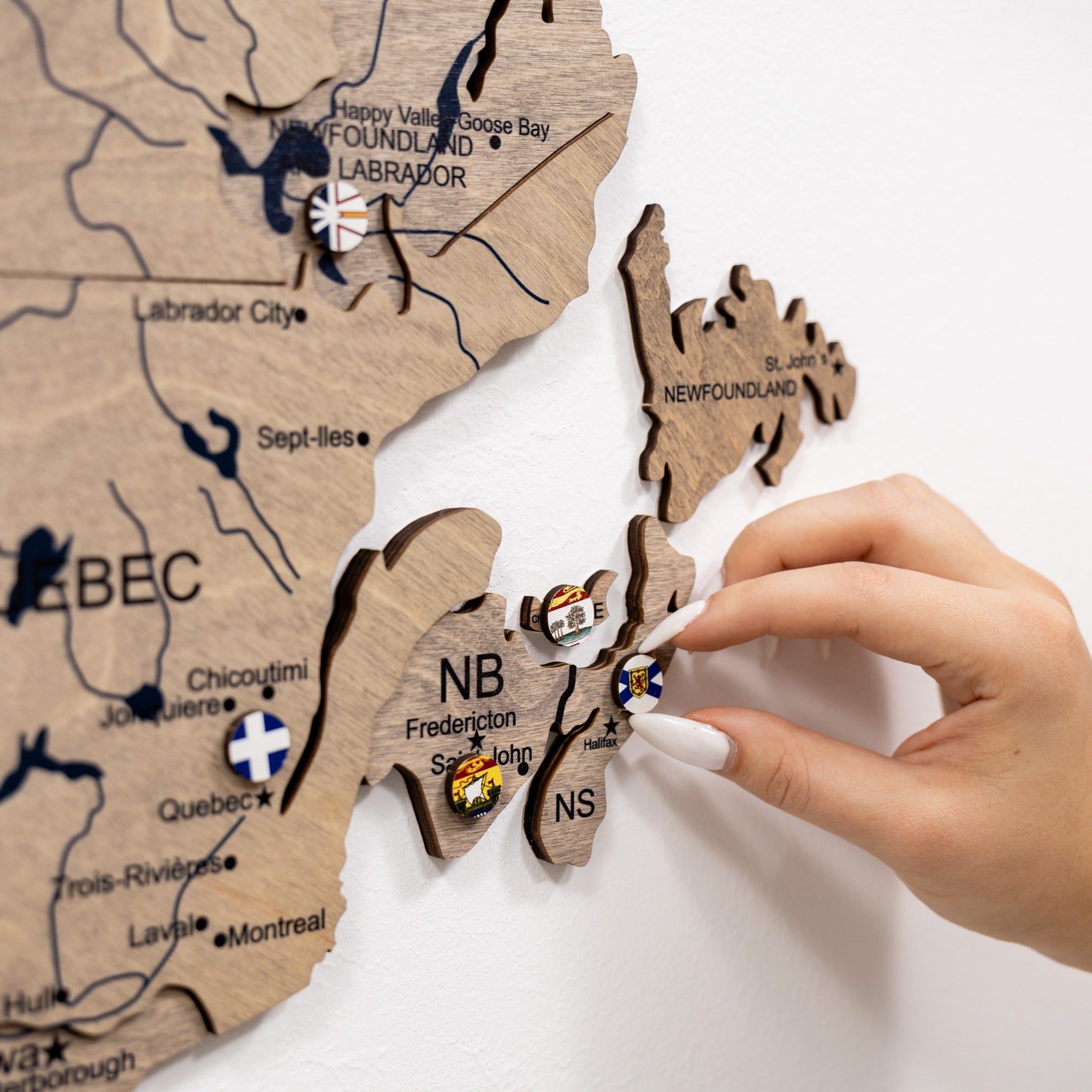 Wooden map of Canada with pins being placed by a hand on a white background