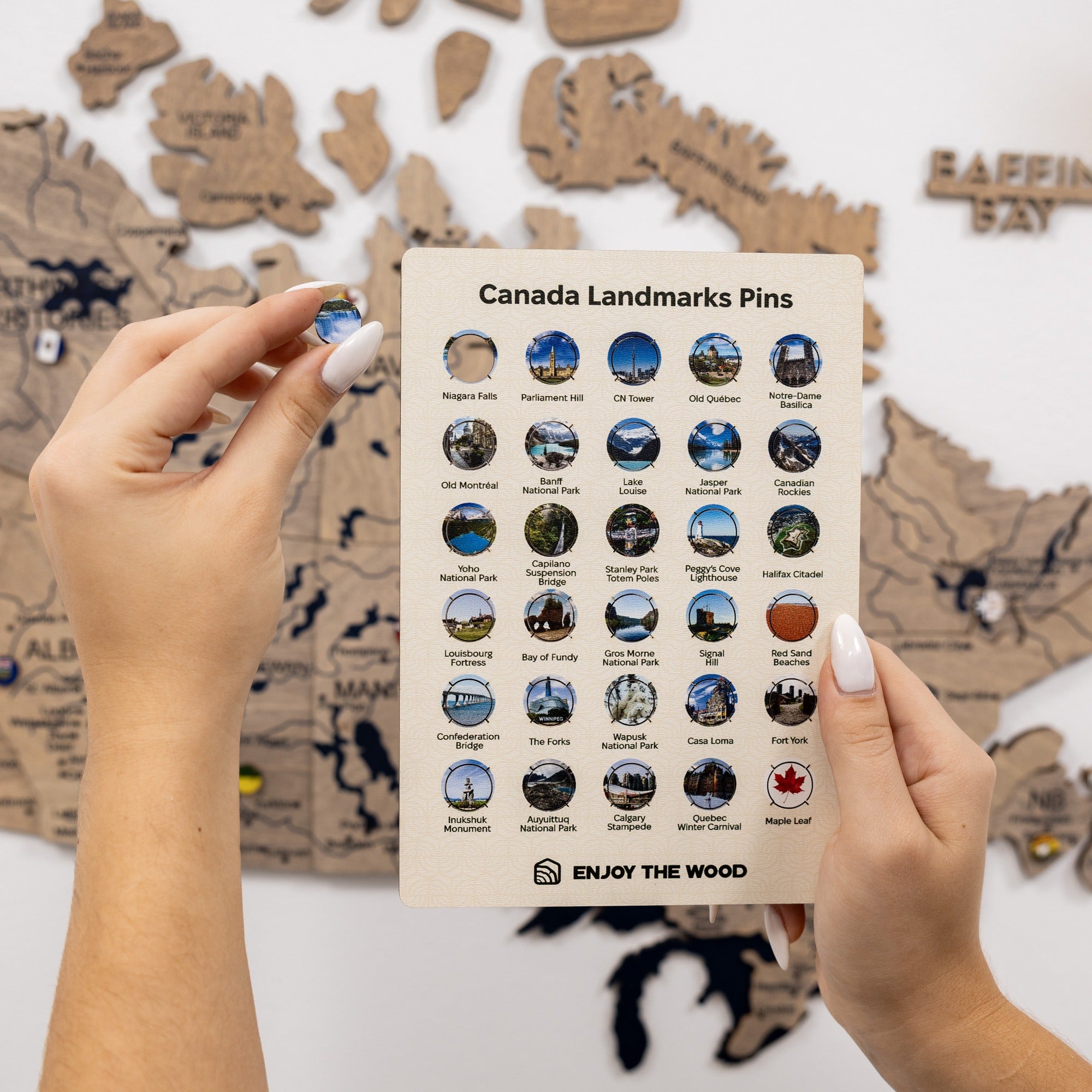 Hand holding a card with Canada landmarks pins against a wooden map background