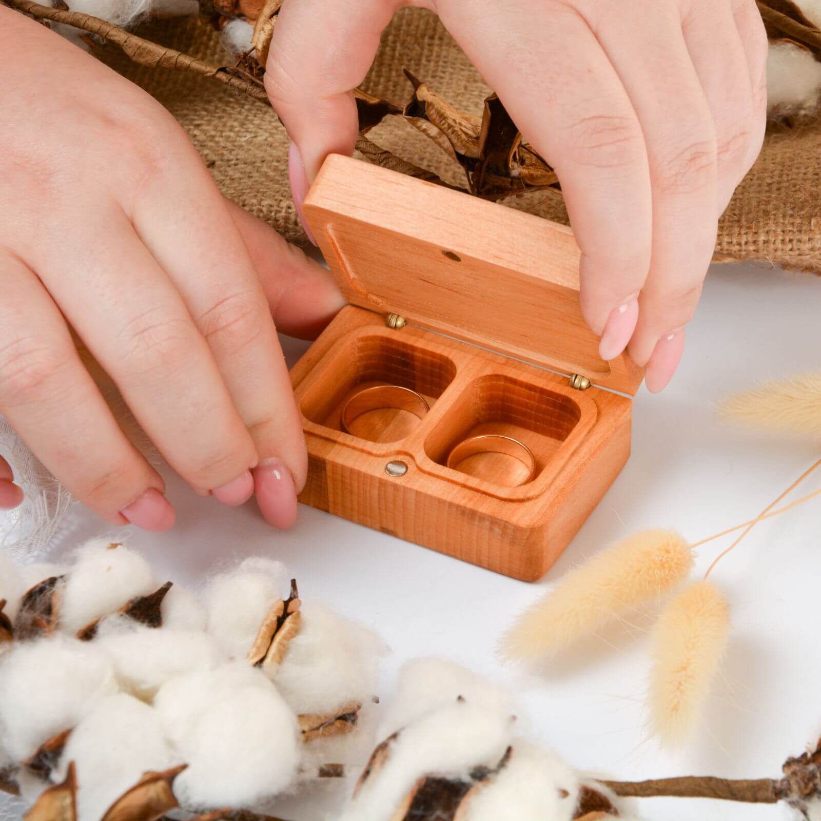 Hands holding wooden ring box with rustic cotton background.