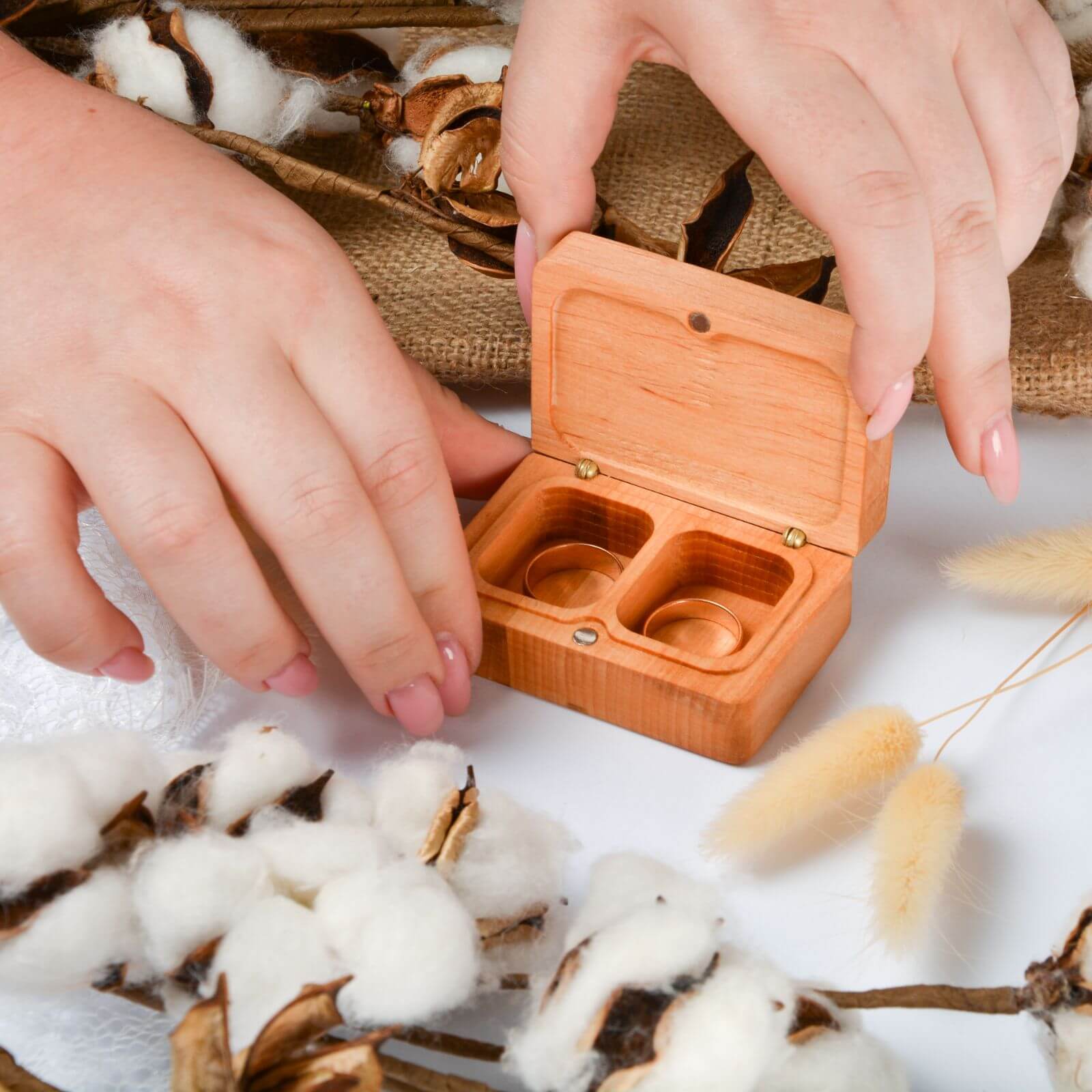 Woman’s hands opening wooden ring box with two wedding rings.