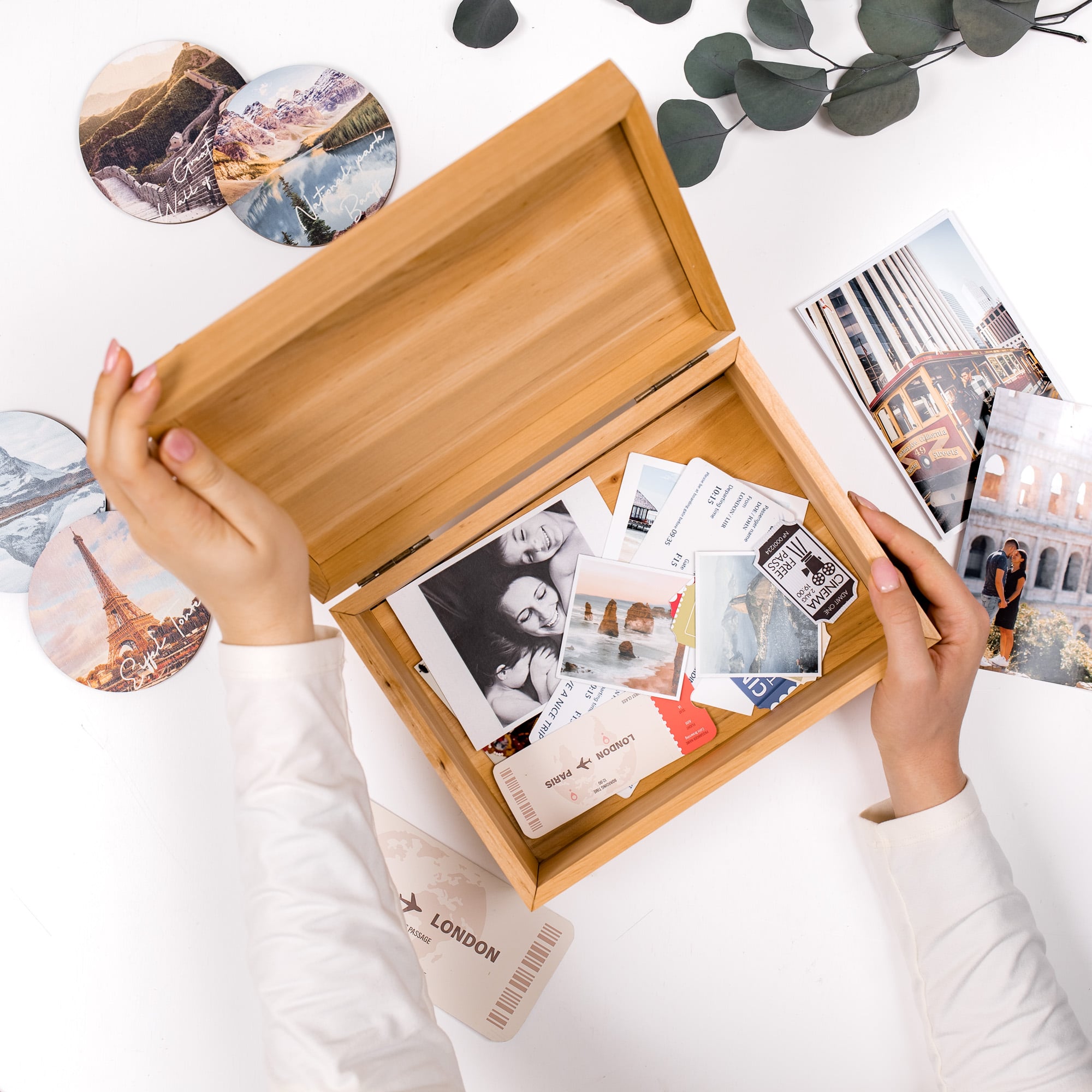 Person opening a wooden photo album with travel-themed photos on a white surface.