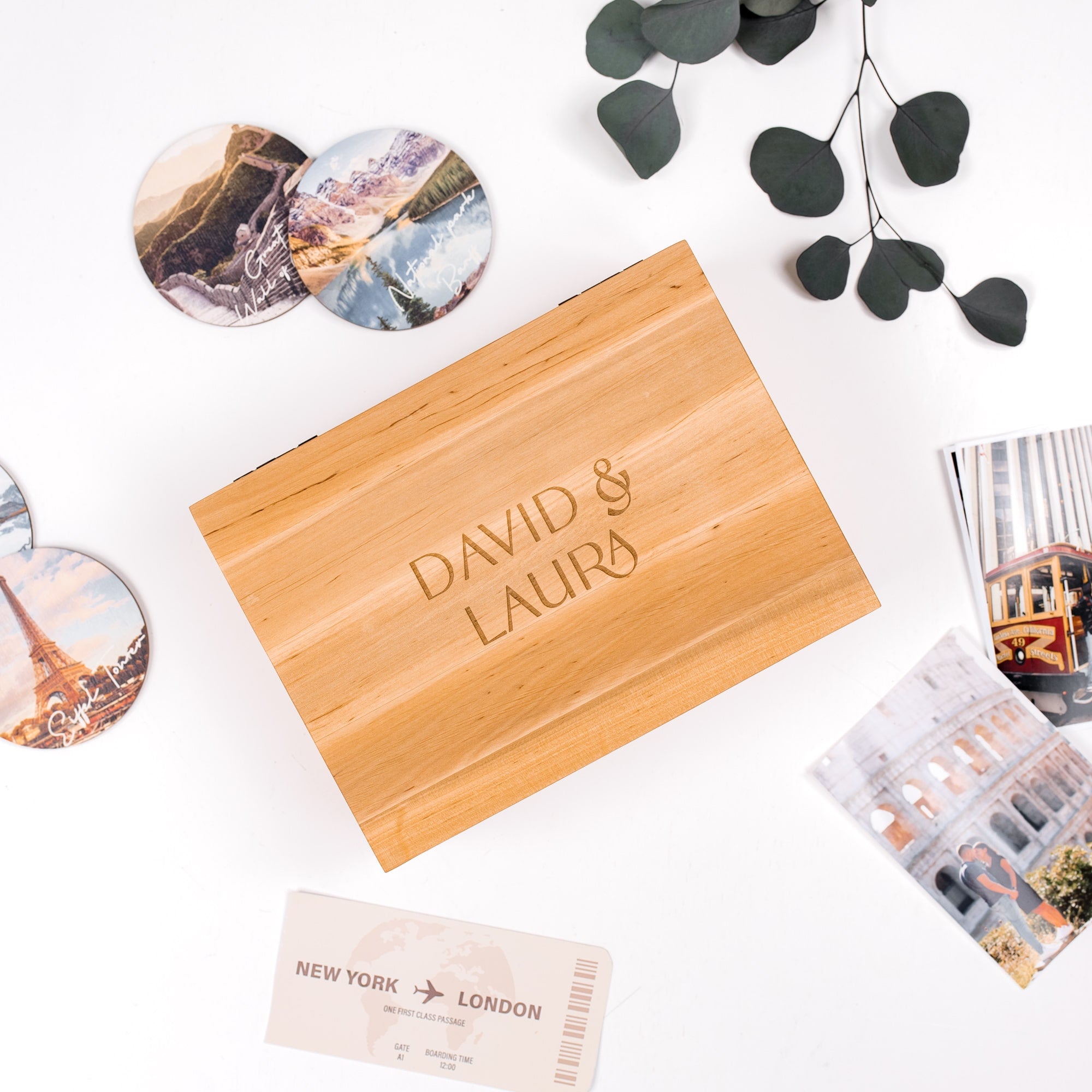 Wooden box with 'DAVID & LAURA' engraving, travel-themed items on a white background