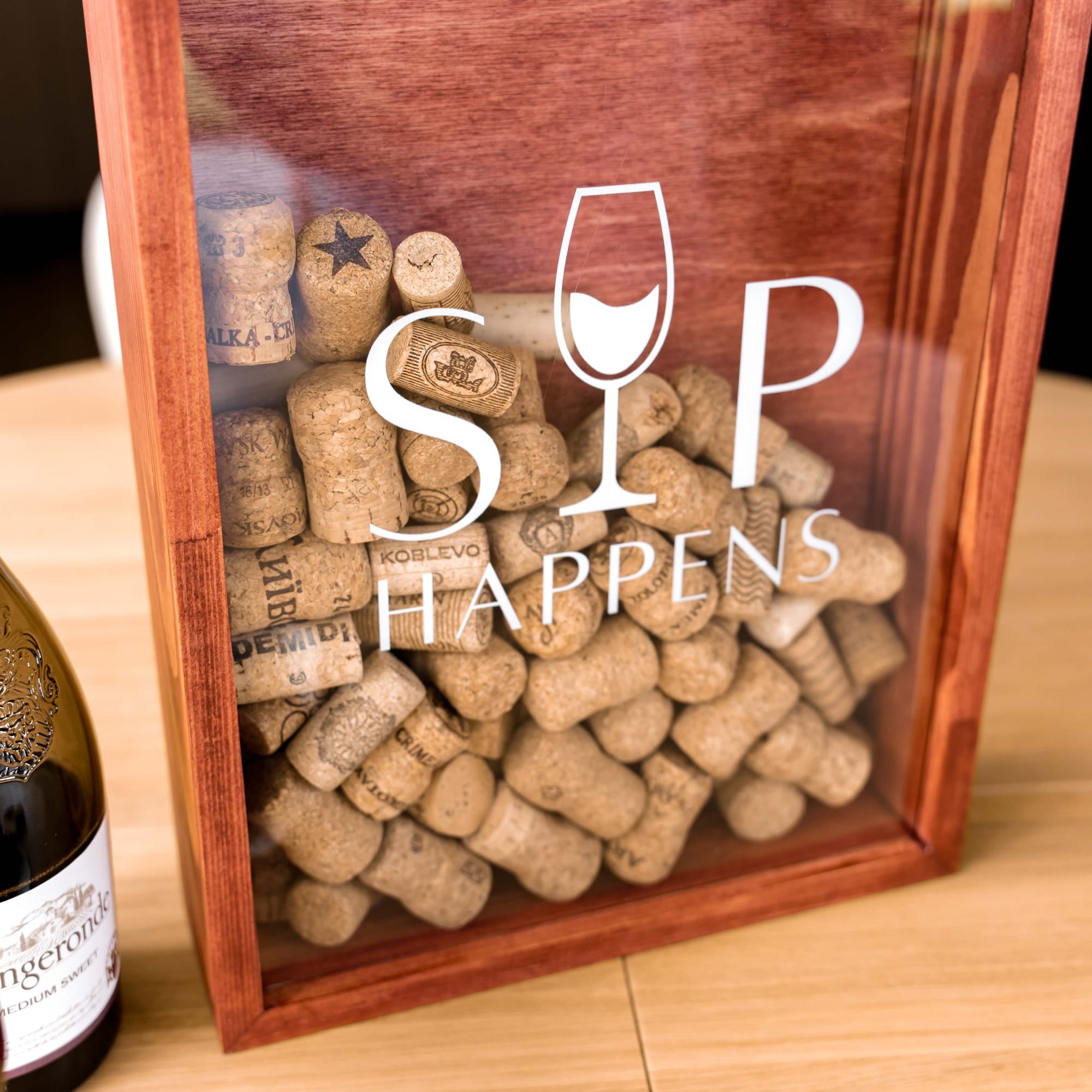 A wooden gift box with a clear front panel filled with assorted wine and spirit corks