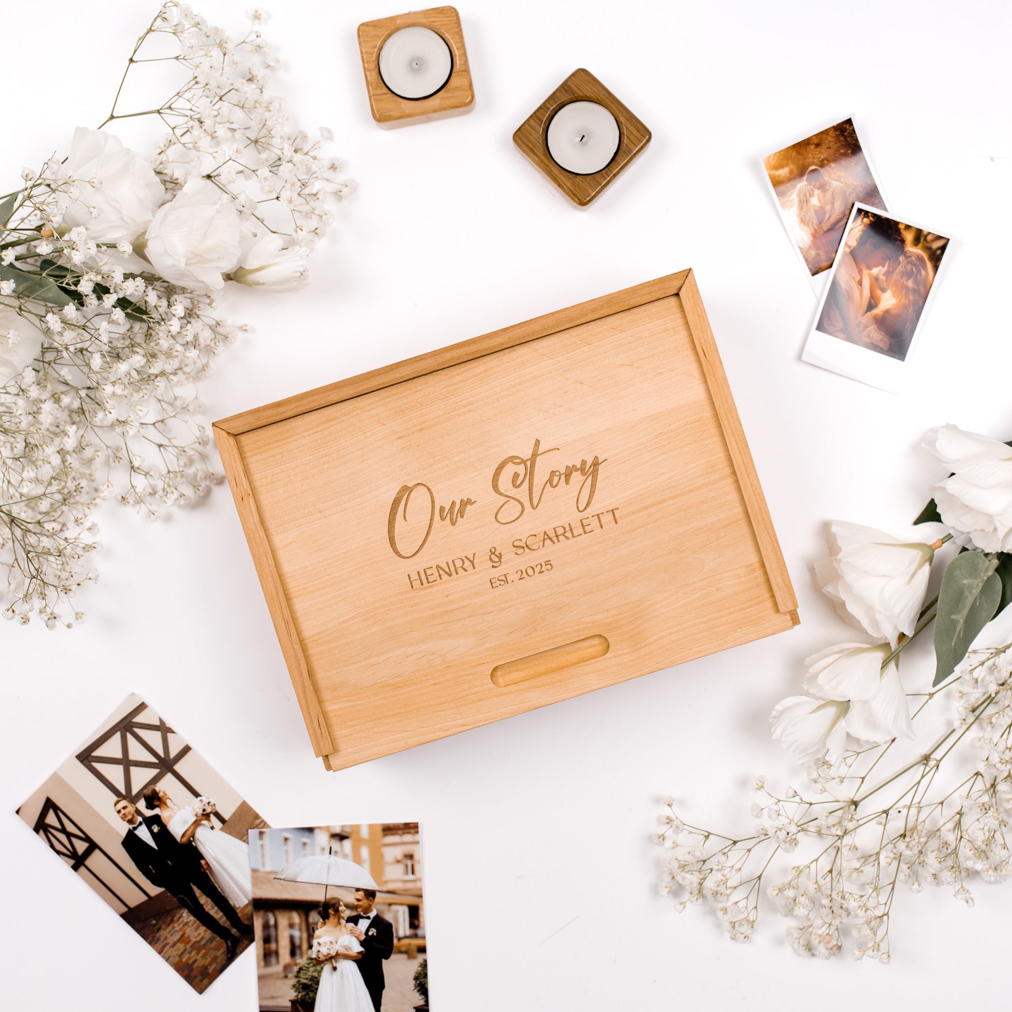 Wooden box with 'Our Story' engraving on a white surface with flowers and photos.
