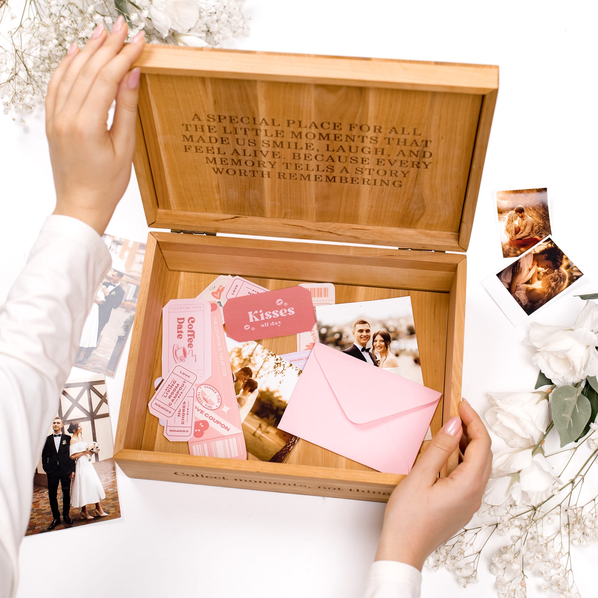 Wooden box with engraved text, photos, and cards held by hands on a white background