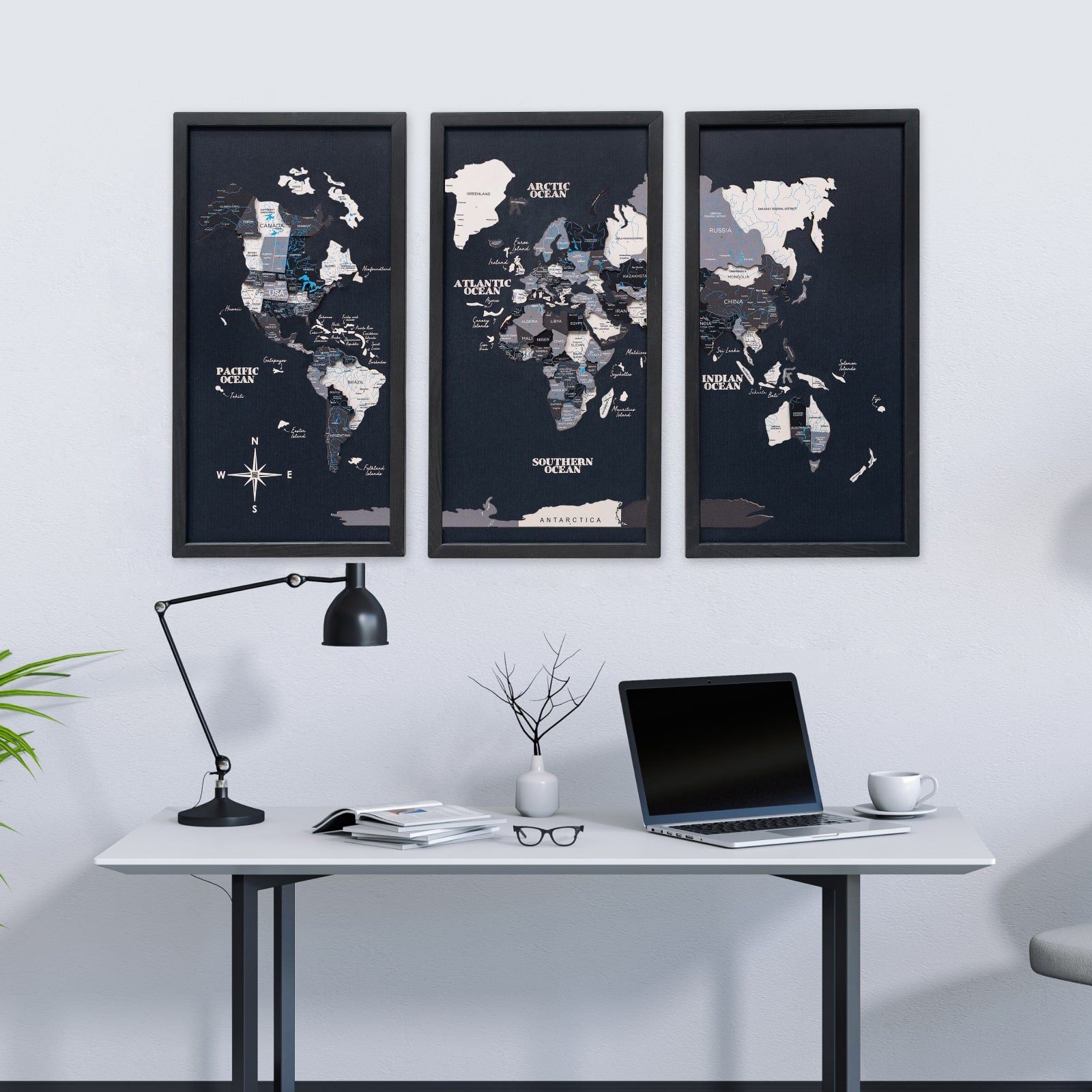 World map posters on a wall above a desk with a laptop and lamp.