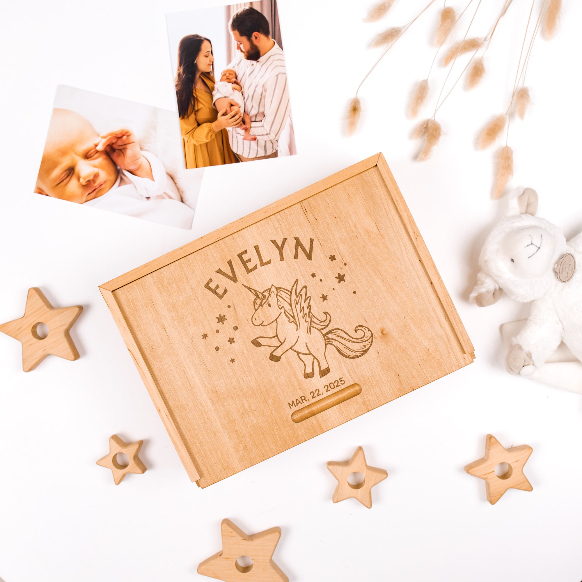 Wooden box with engraved name and date, surrounded by star-shaped objects and a baby photo on a white background.