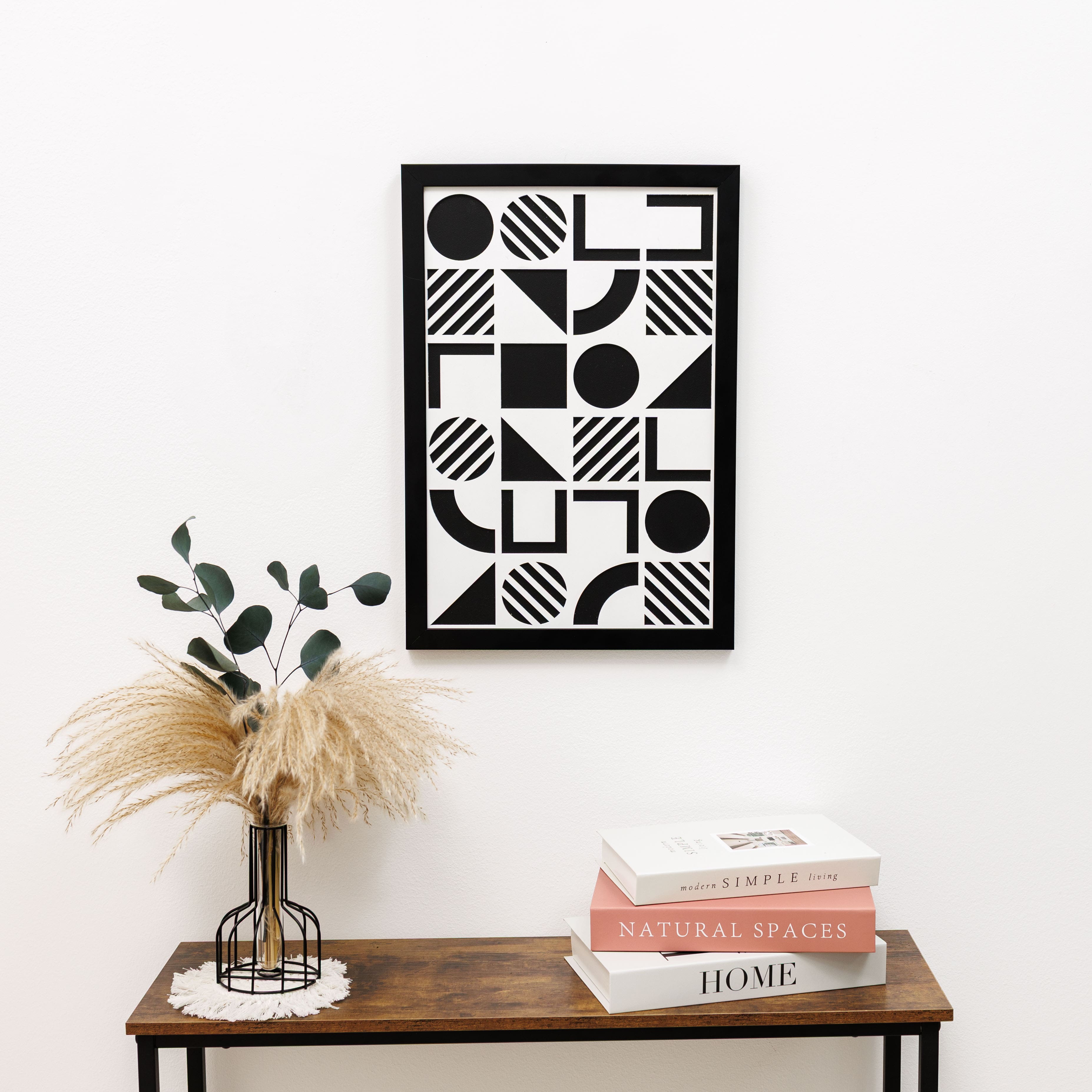 Framed geometric art piece on a wall above a wooden console table with books and a vase.