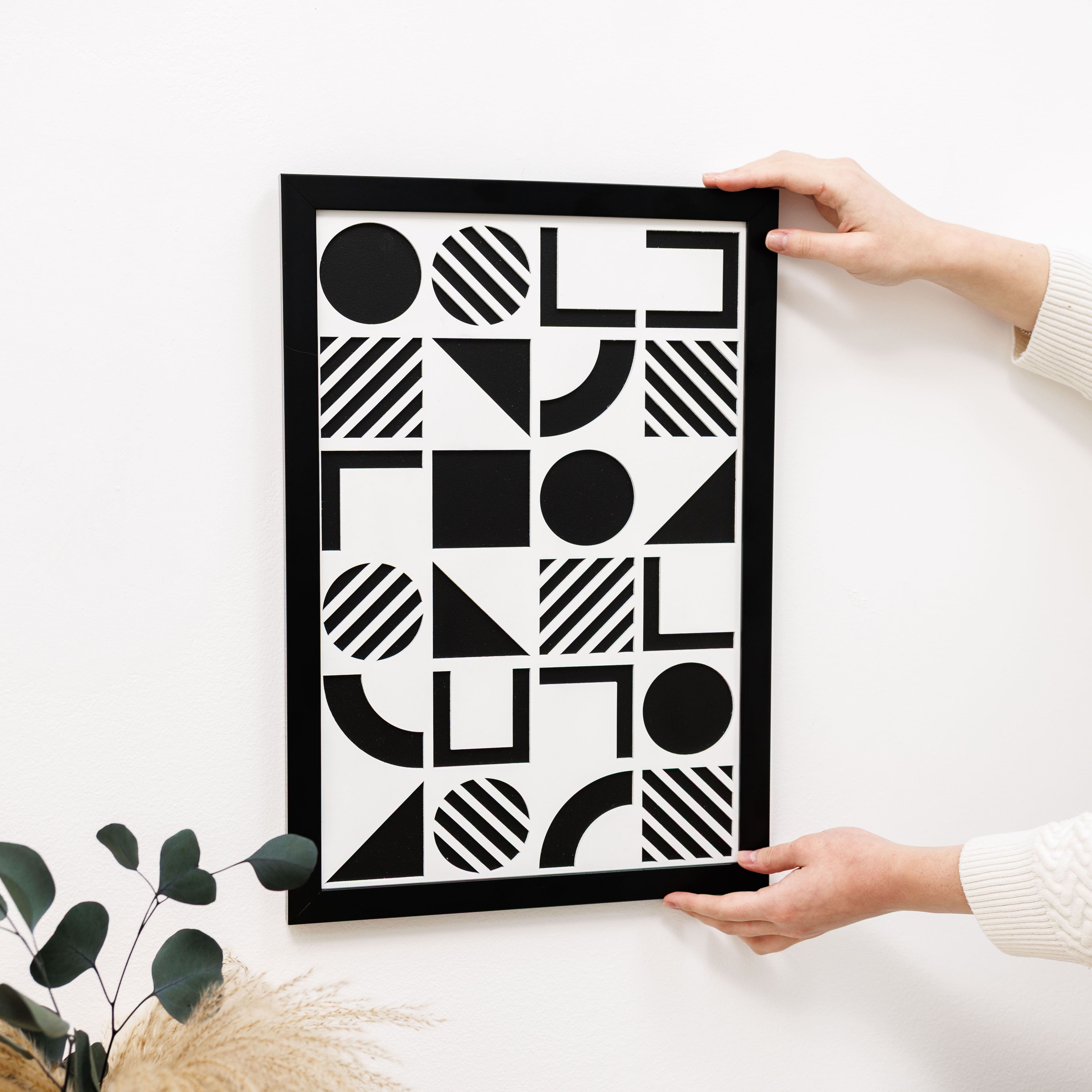 Person holding a framed black and white geometric art print on a light surface.