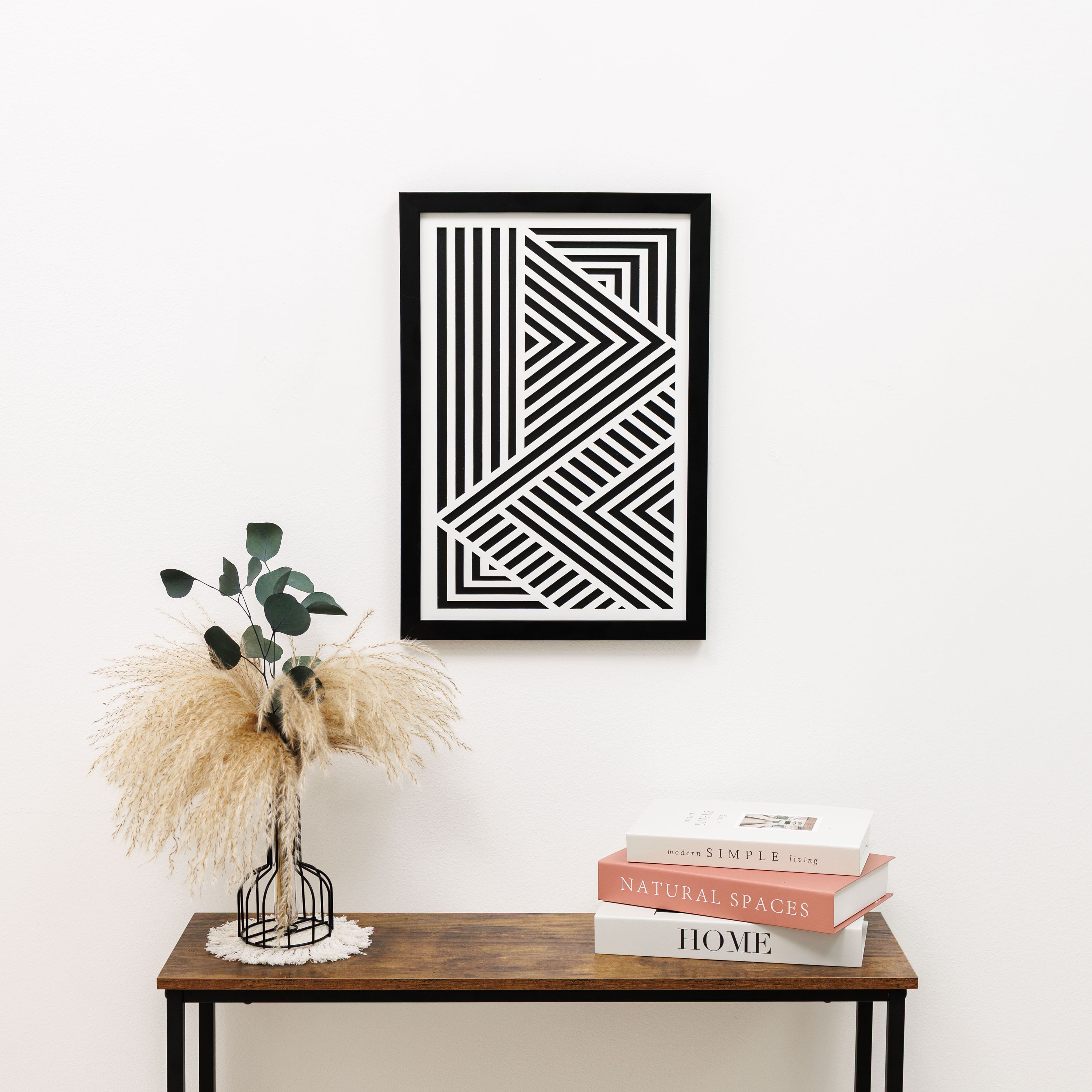Framed geometric art piece on a wall above a wooden table with decorative items.