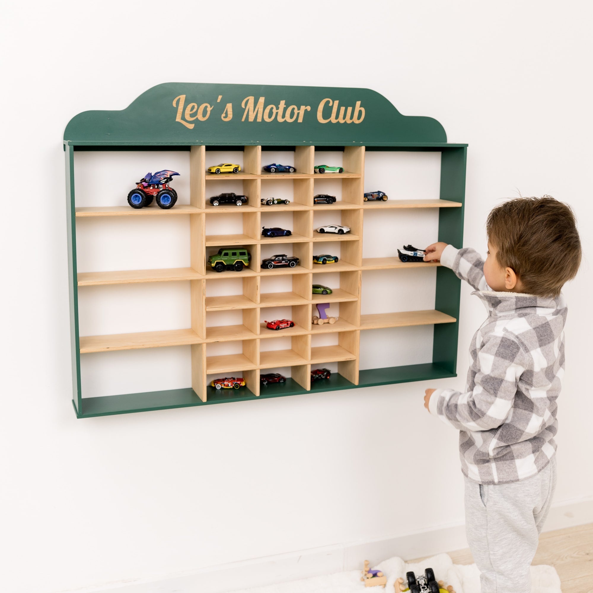 Child playing with toy car display unit named 'Leo's Motor Club' on a white wall.