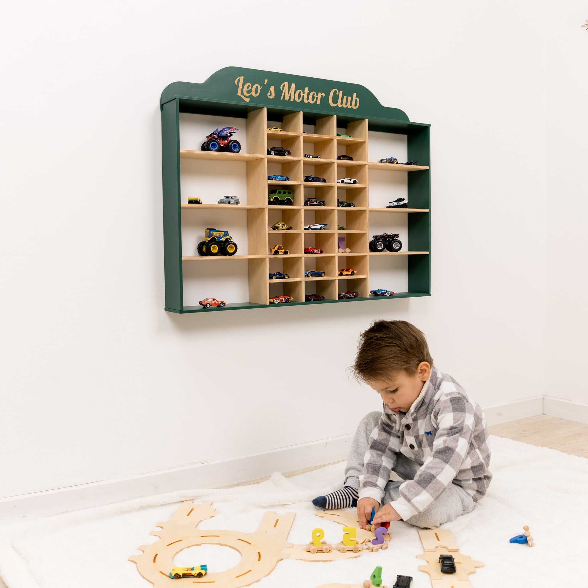 Child playing with toy cars on a wooden floor next to a shelf labeled 'Leo's Motor Club'.
